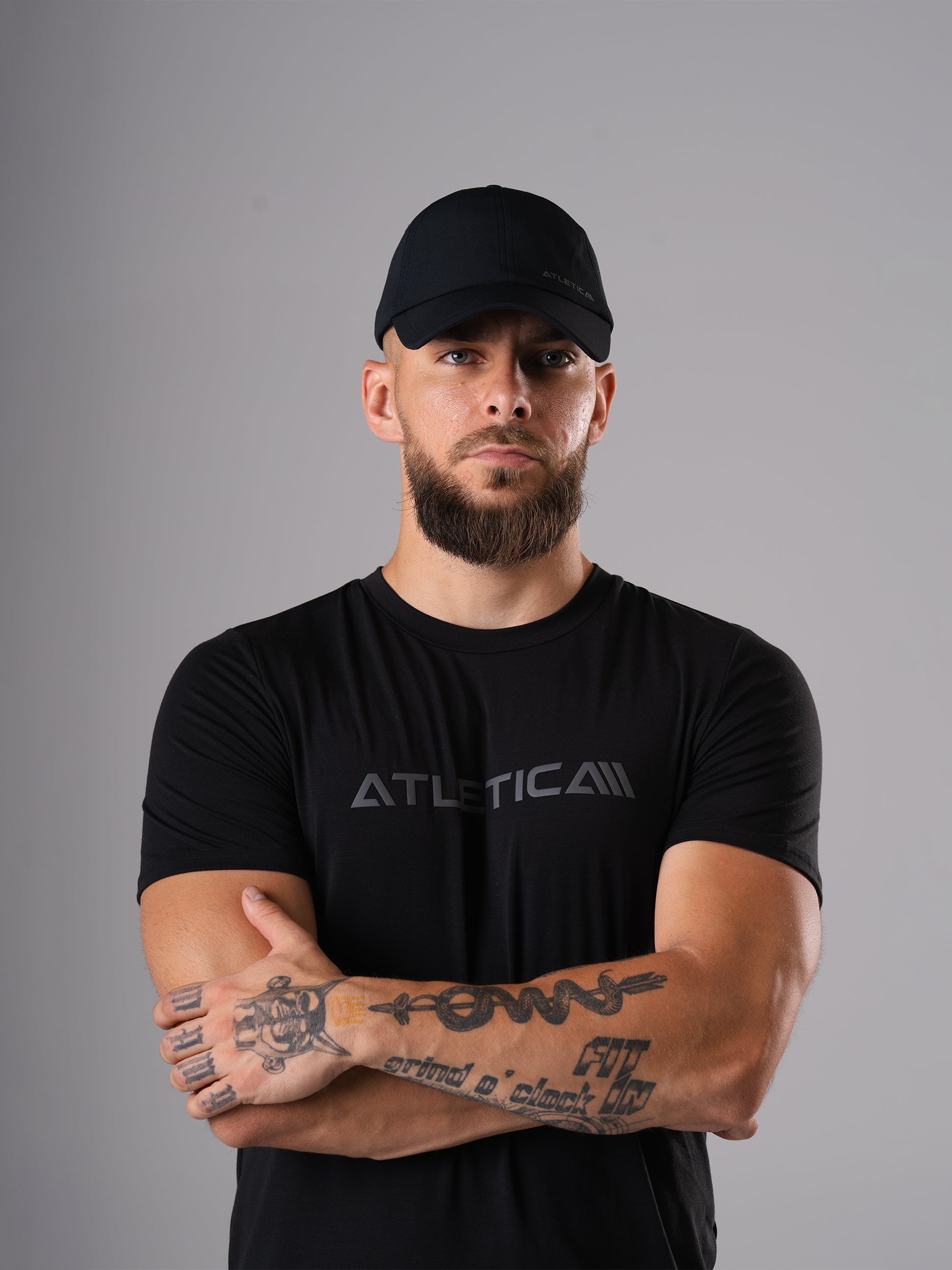 Mann mit verschränkten Armen im schwarzen Merch Flex Train T-Shirt und Cool Cap von Atletica