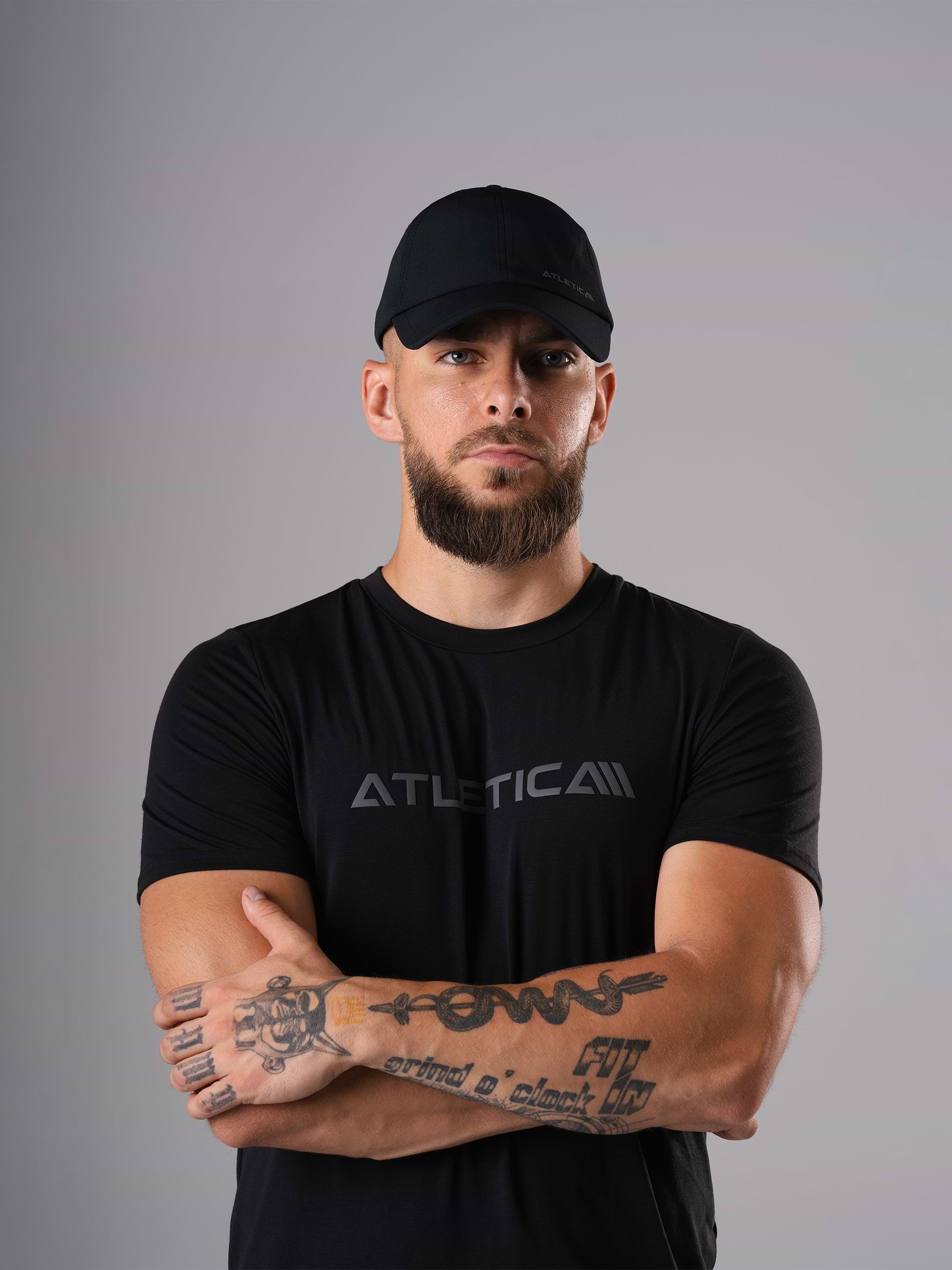 Mann mit verschränkten Armen im schwarzen Merch Flex Train T-Shirt und Cool Cap von Atletica