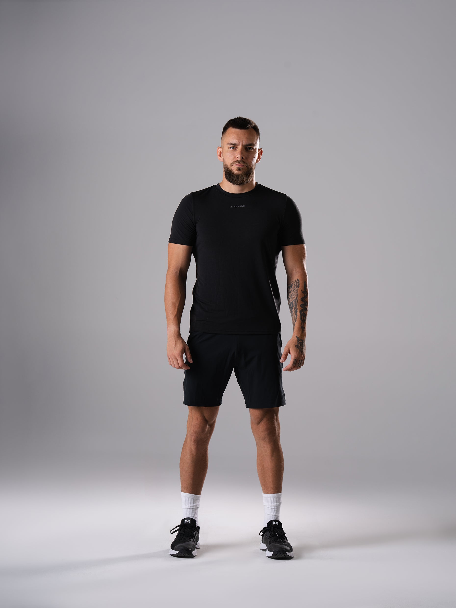 Mann im Flex Train T-Shirt in Schwarz von Atletica mit schwarzen Shorts, Ganzkörperansicht