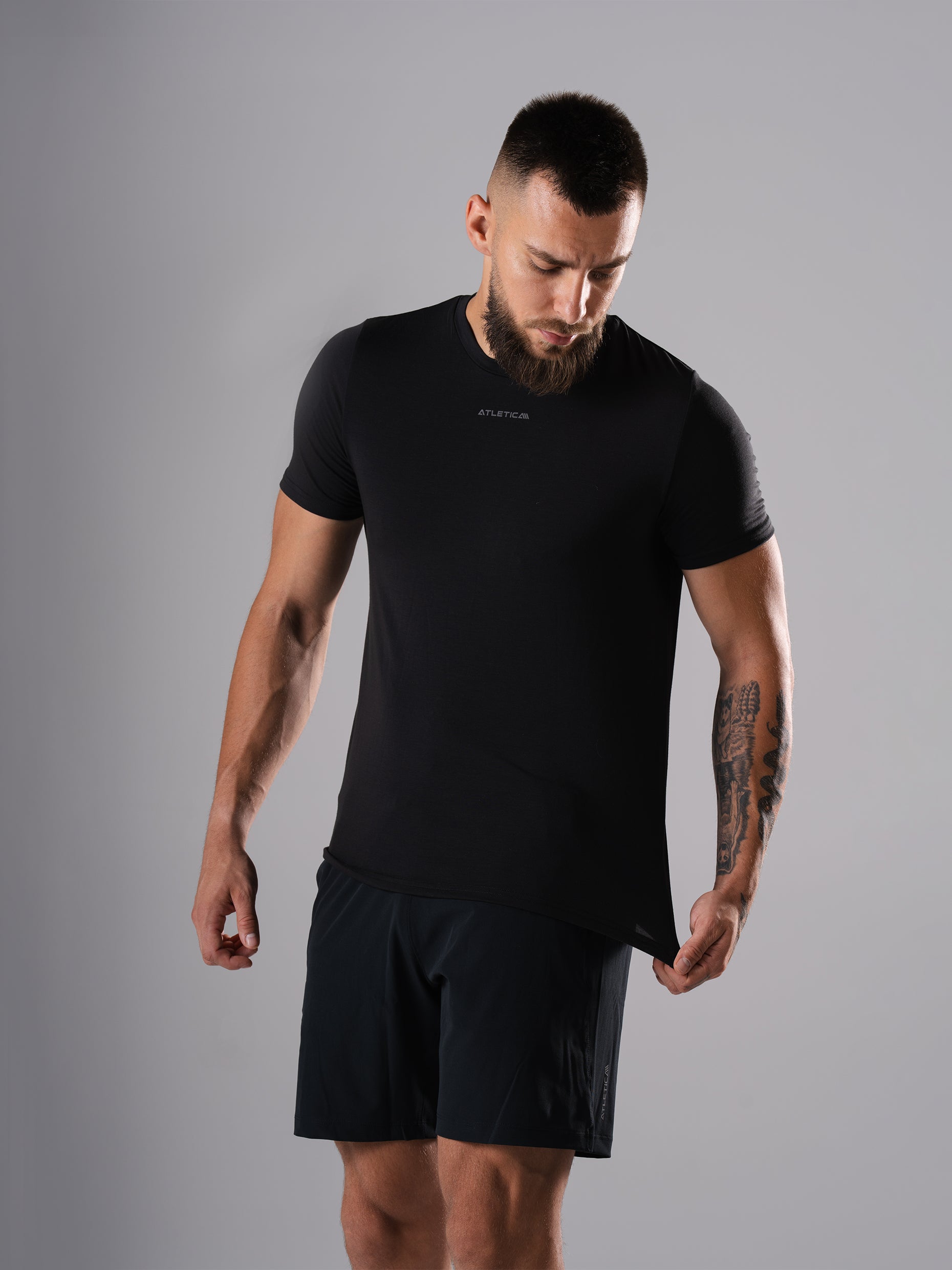 Mann zieht am Saum des Flex Train T-Shirts in Schwarz von Atletica
