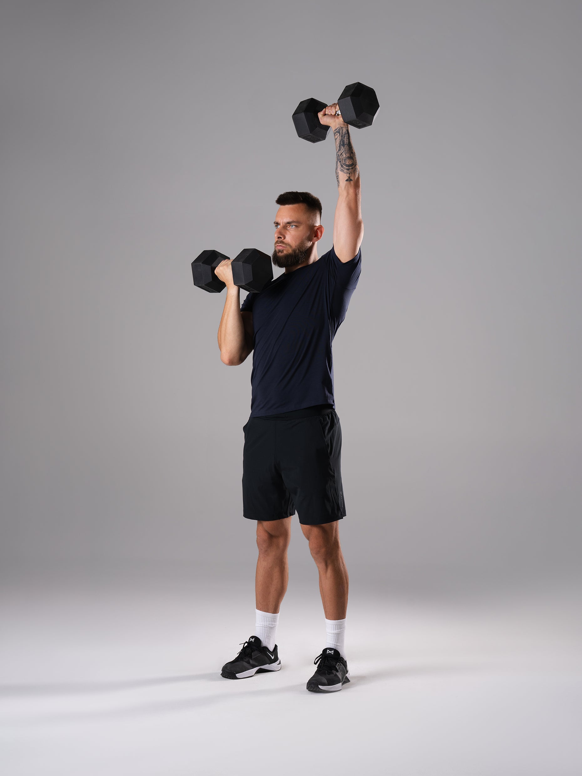 Mann im Flex Train T-Shirt in Dark Navy von Atletica beim einarmigen Schulterdrücken mit Hexagon Kurzhantel