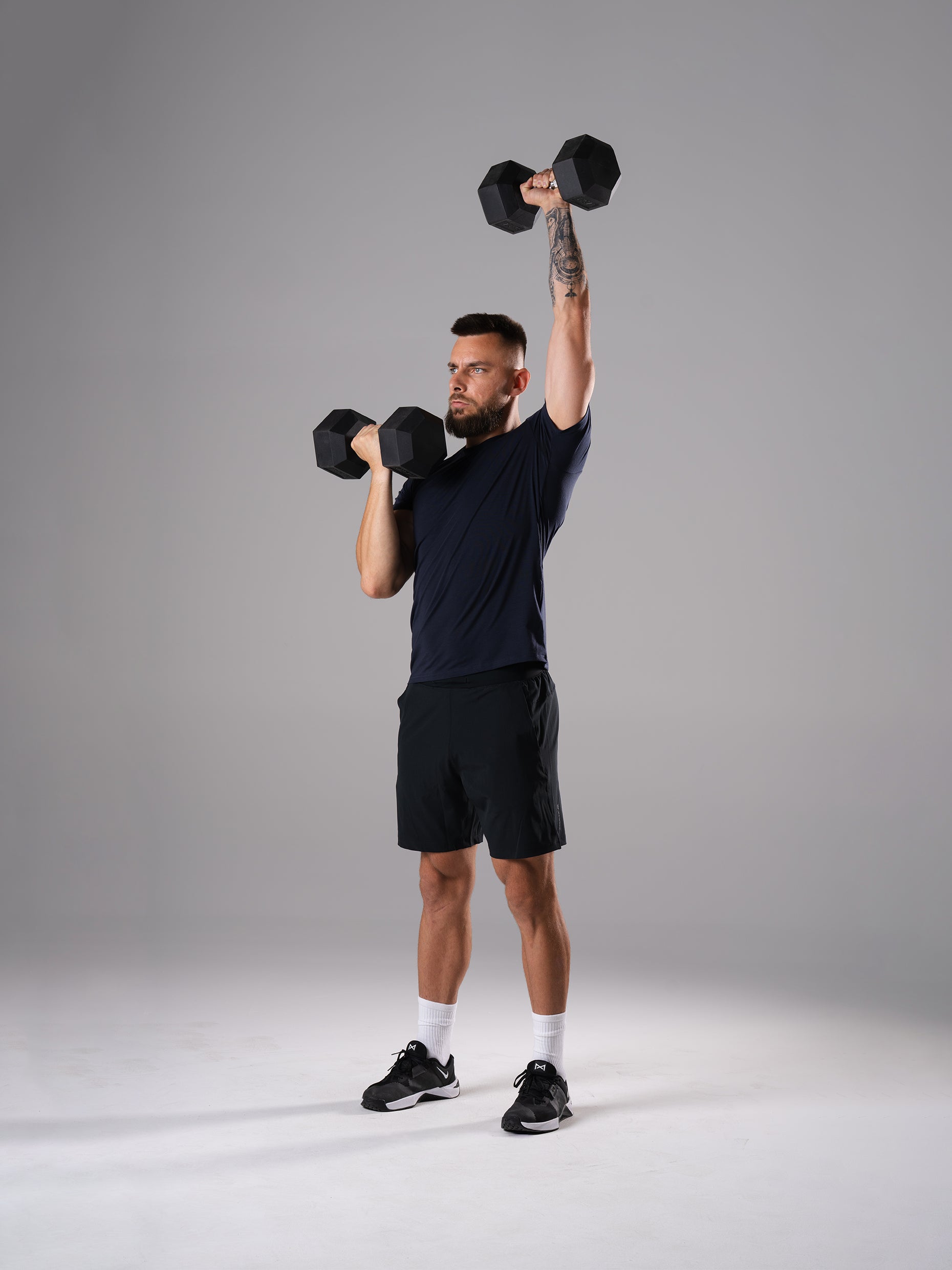 Mann im Flex Train T-Shirt in Dark Navy von Atletica beim einarmigen Schulterdrücken mit Hexagon Kurzhantel