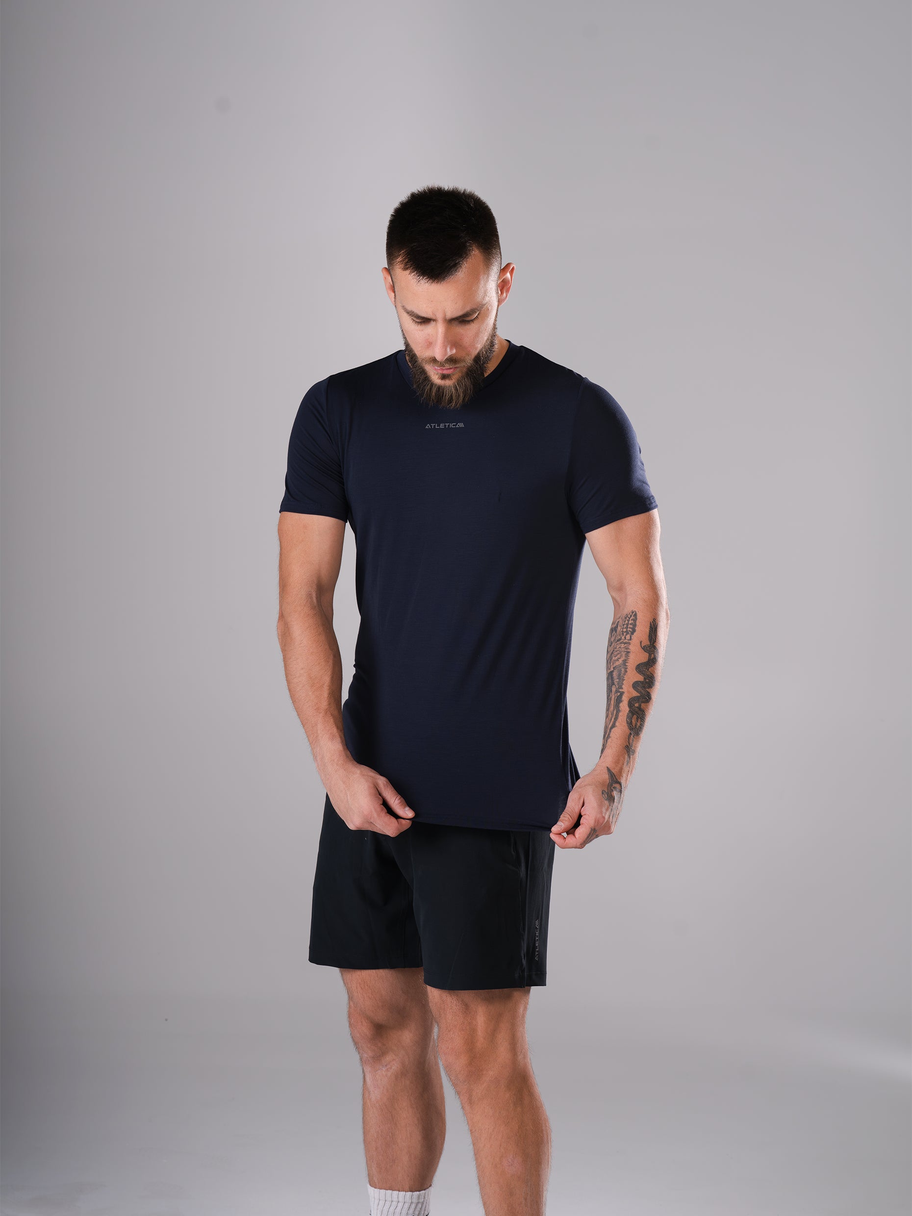 Mann zieht am Saum des Flex Train T-Shirt in Dark Navy von Atletica