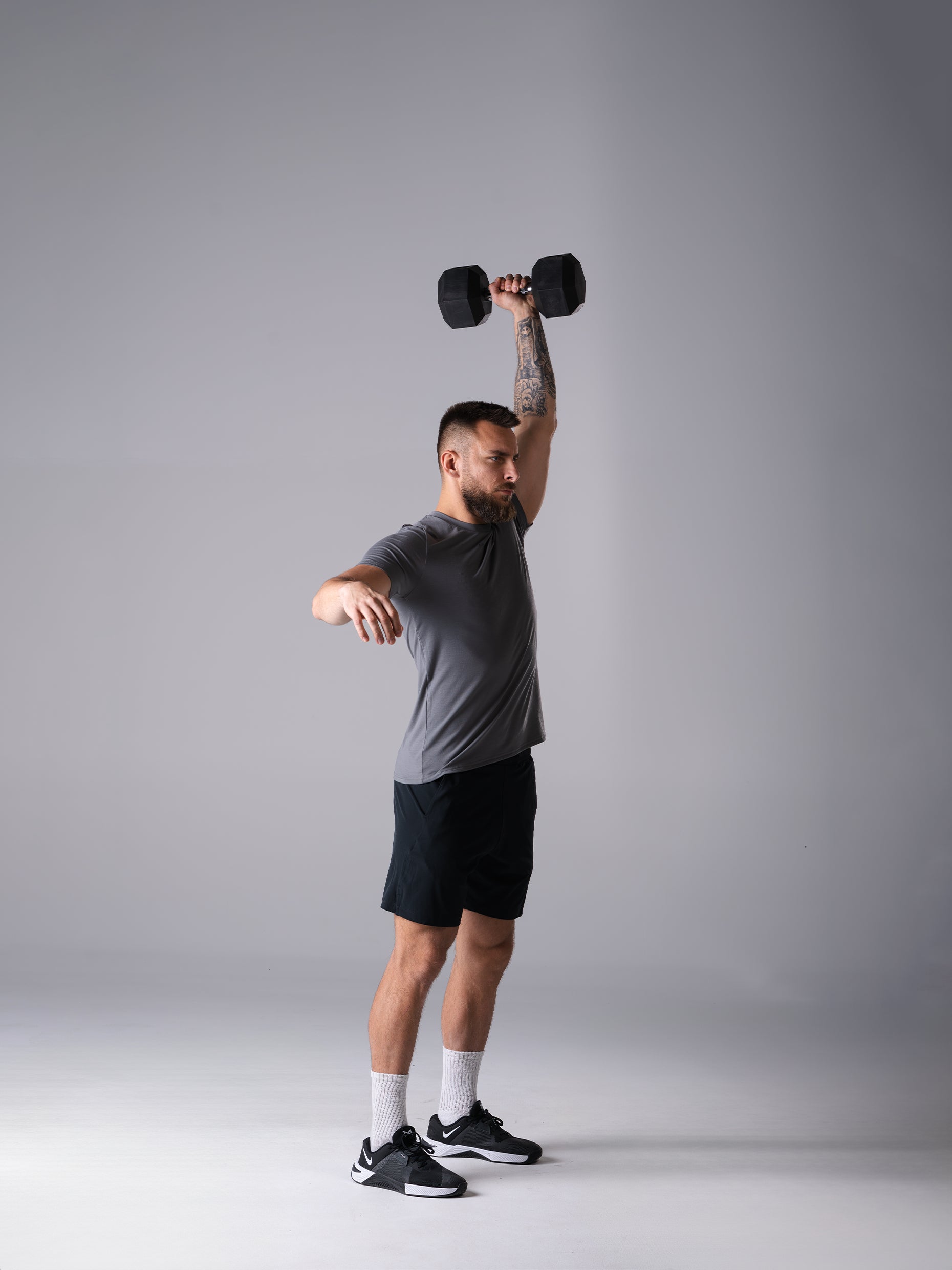 Mann im Flex Train T-Shirt in CastleRock Grey von Atletica beim einarmigen Schulterdrücken mit Hexagon Kurzhantel
