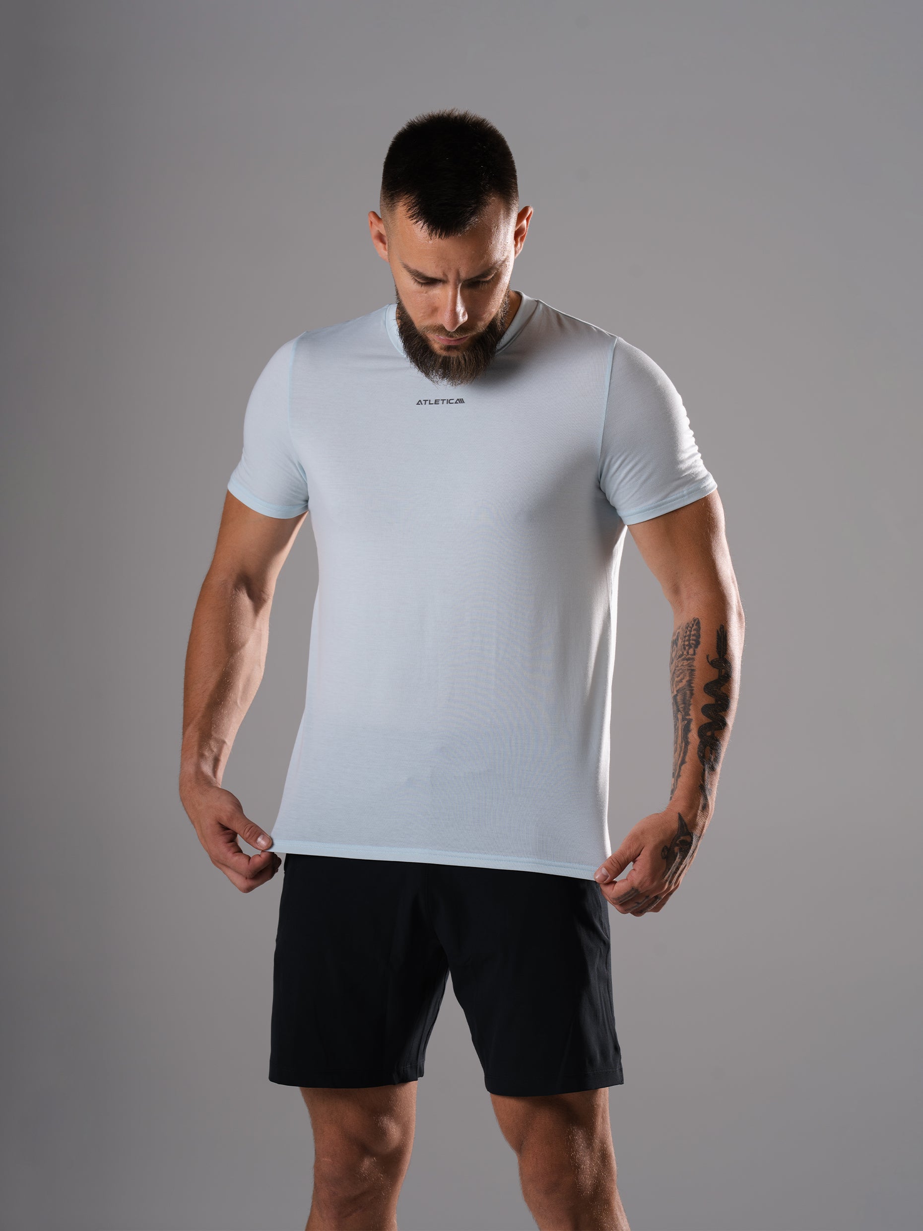 Mann zieht am Saum des Flex Train T-Shirts in Ice Blue von Atletica