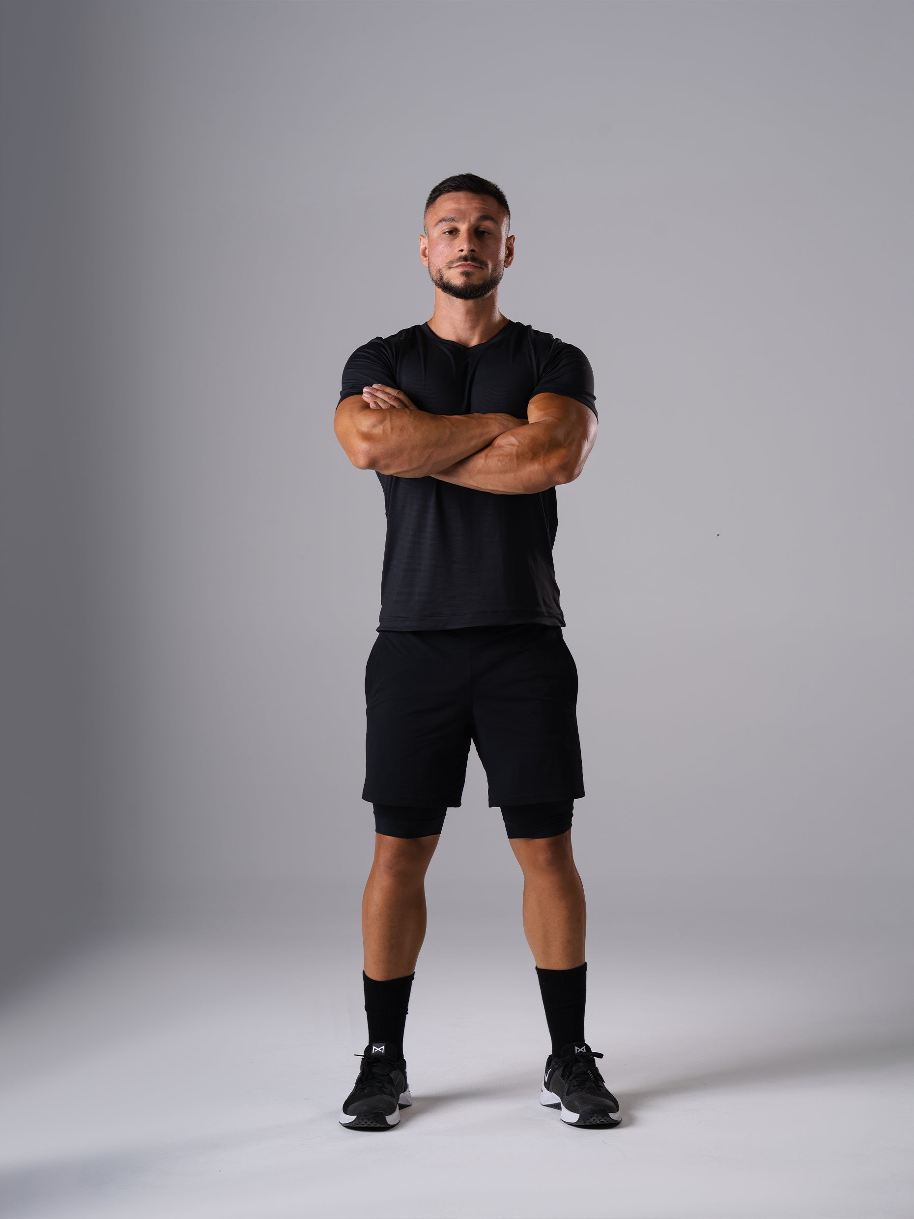Mann in den Hard Lift Shorts und T-Shirt in Schwarz von Atletica mit verschränkten Armen, Ganzkörperansicht