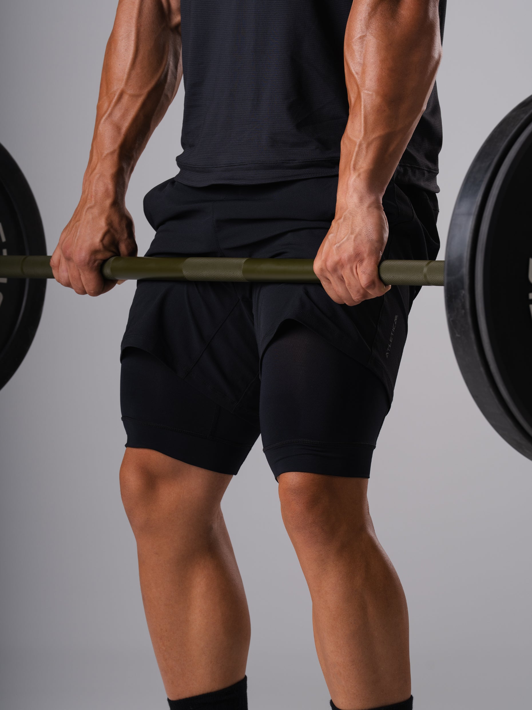 Mann in den schwarzen Hard Lift Shorts von Atletica hält eine beladene Langhantel beim Kreuzheben