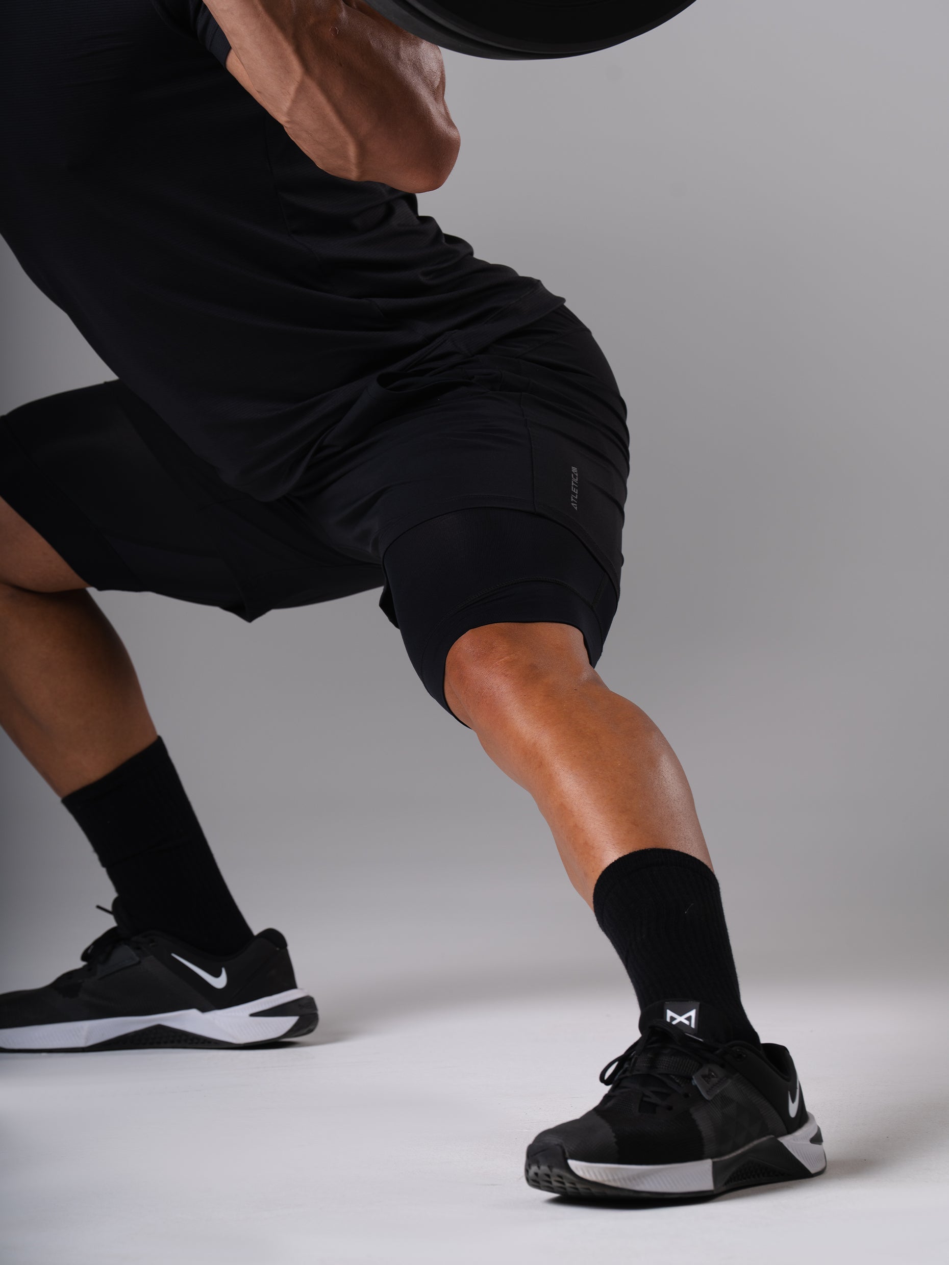 Mann in den schwarzen Hard Lift Shorts von Atletica bei der Kniebeuge mit Langhantel