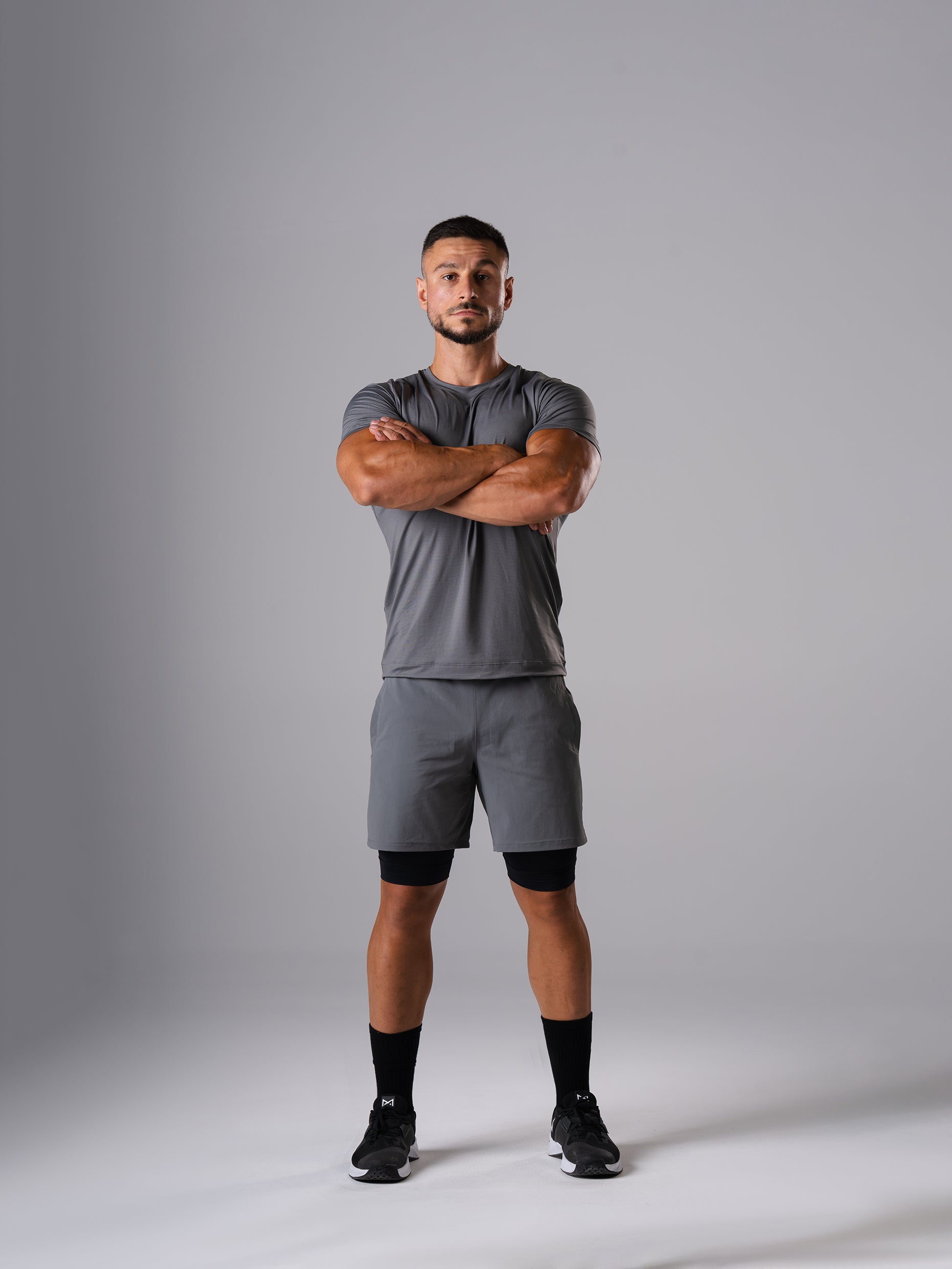 Ganzkörperansicht: Mann in den Hard Lift Shorts in CastleRock Grey von Atletica mit verschränkten Armen