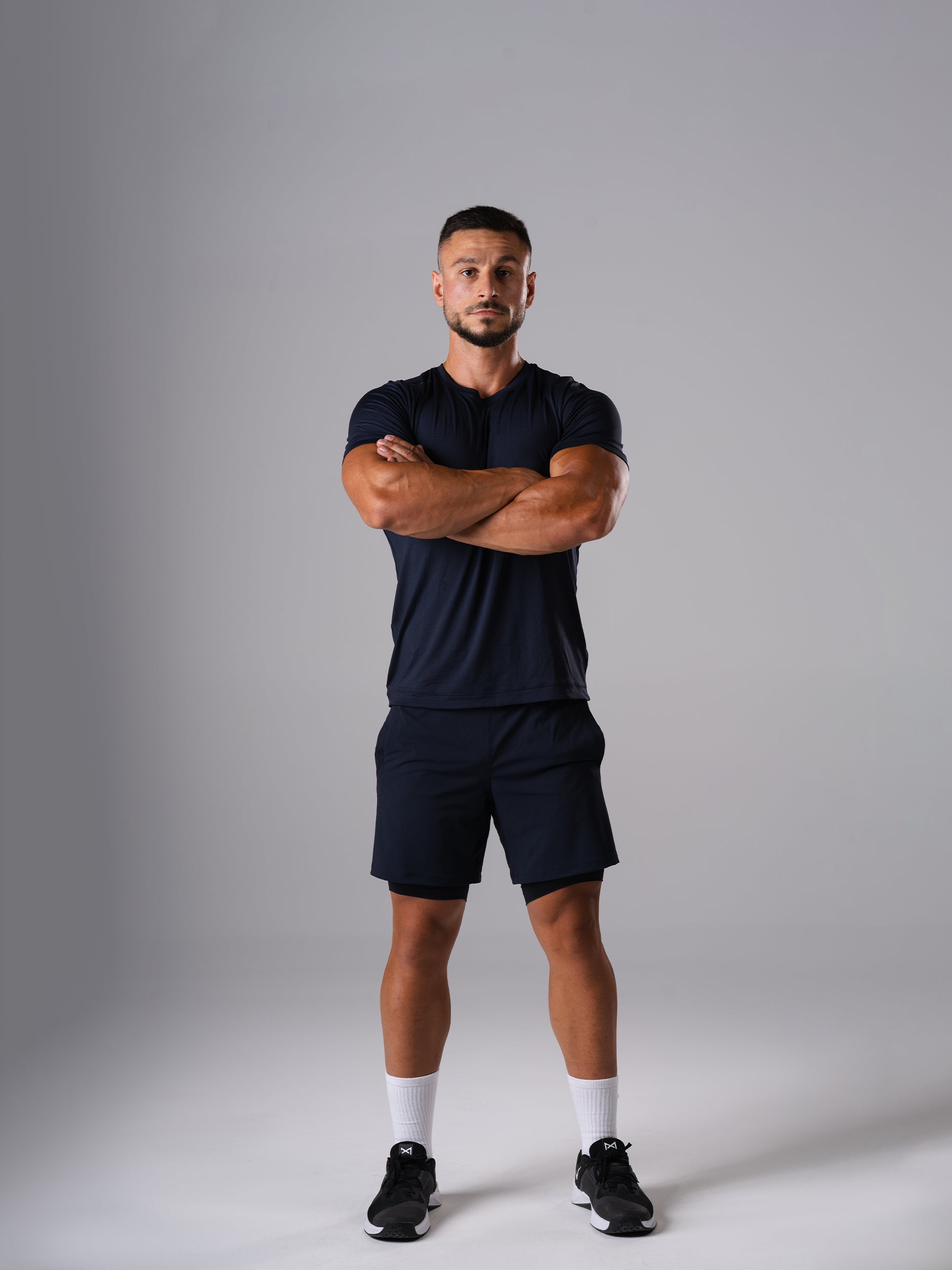 Mann in den Hard Lift Shorts und Hard Lift Shirt in Dark Navy von Atletica mit verschränkten Armen, Ganzkörperansicht