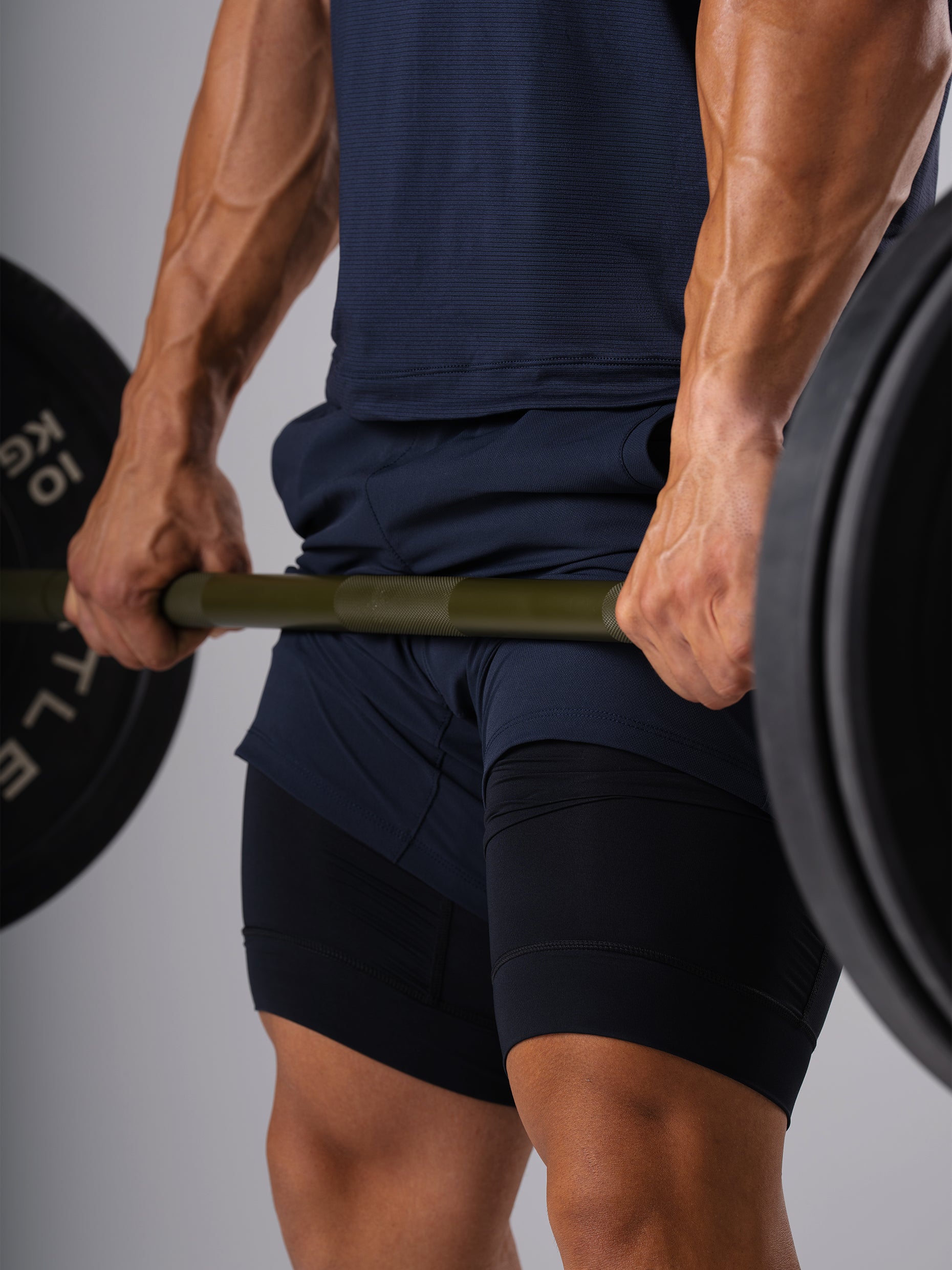 Mann in den Hard Lift Shorts in Dark Navy von Atletica hält eine beladene Langhantel beim Kreuzheben