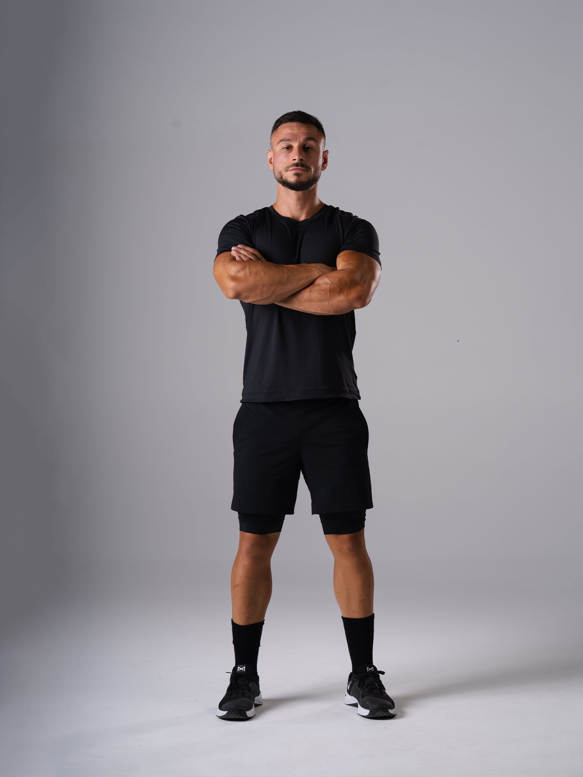 Ganzkörperansicht: Mann im schwarzen Hard Lift T-Shirt von Atletica mit verschränkten Armen
