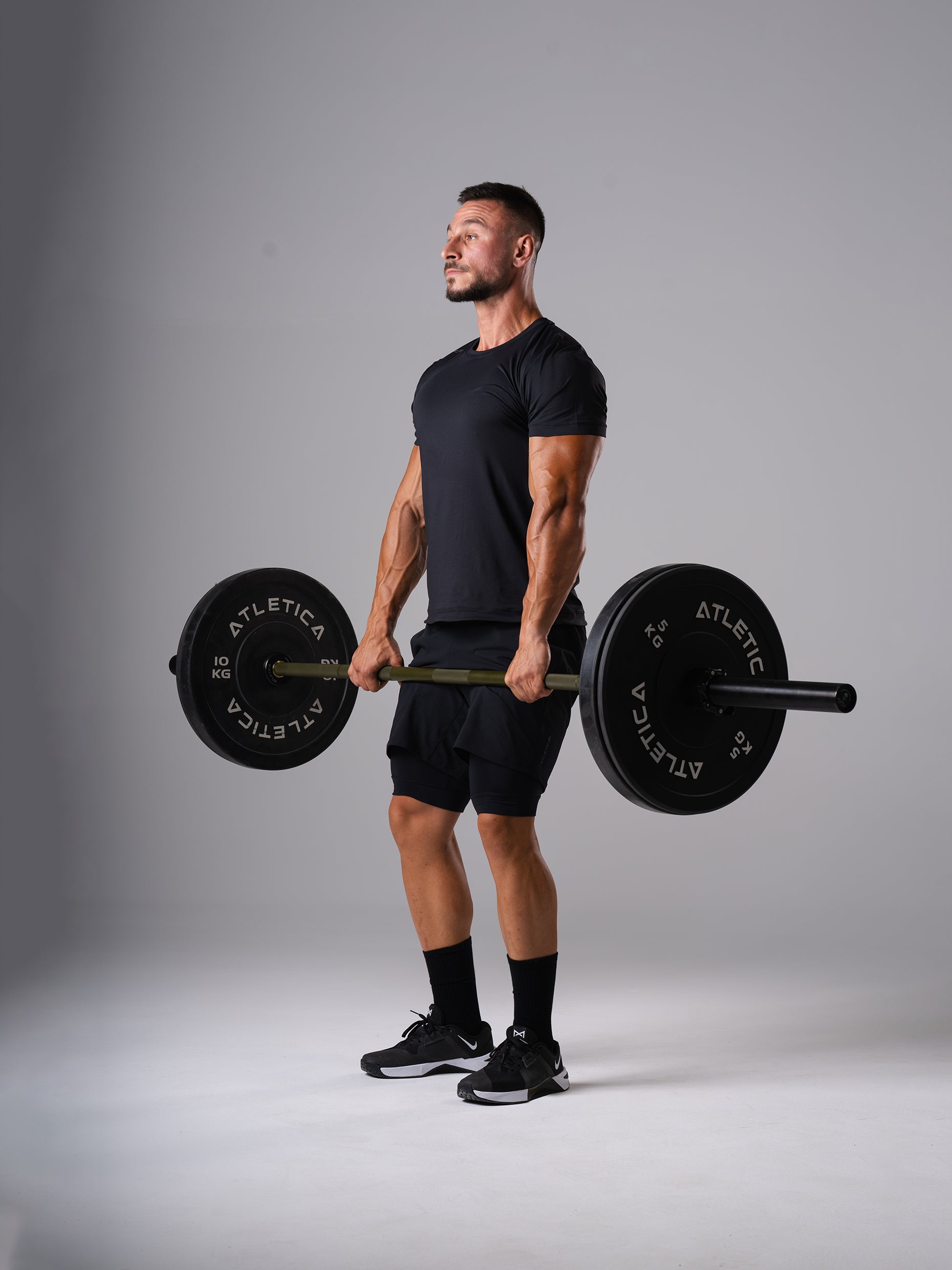 Mann im schwarzen Hard Lift T-Shirt von Atletica hält eine beladene Langhantel beim Kreuzheben