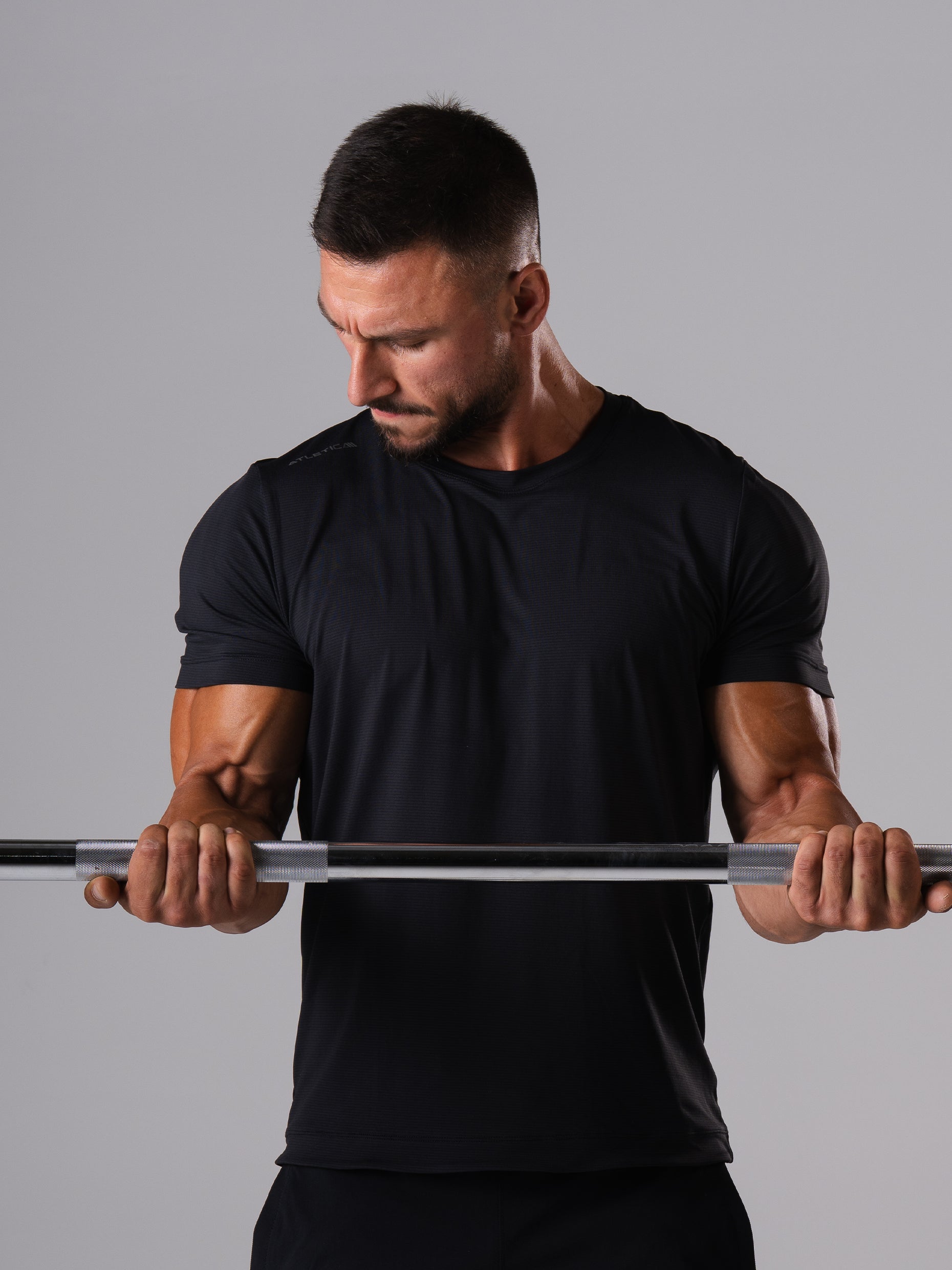 Mann im schwarzen Hard Lift T-Shirt von Atletica greift eine Langhantelstange beim Krafttraining