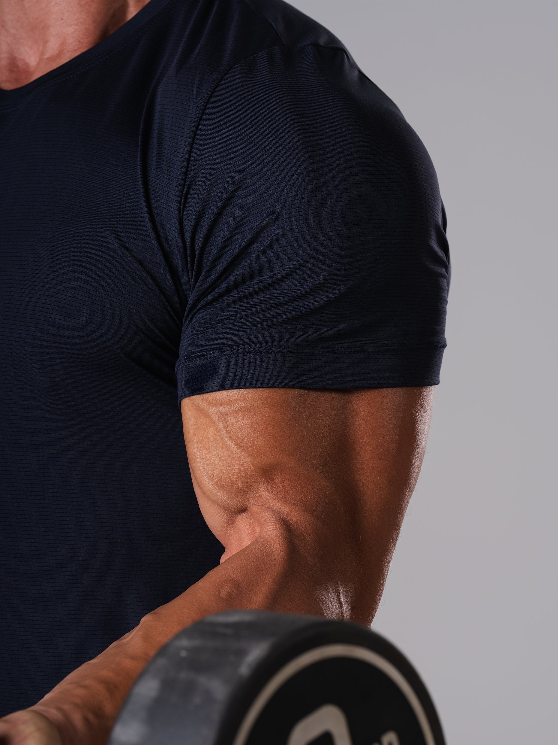 Nahaufnahme des Ärmels am Hard Lift T-Shirt in Dark Navy von Atletica beim Halten einer Hantelscheibe