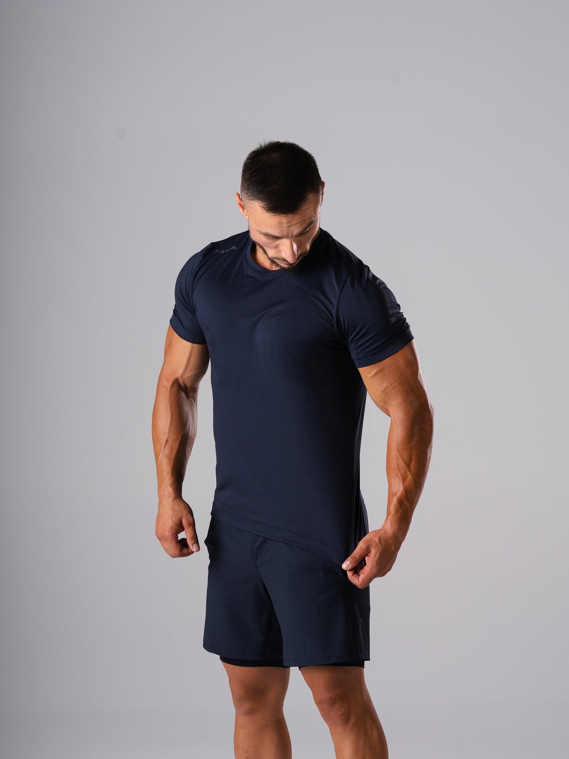 Mann zieht am Saum des Hard Lift T-Shirts in Dark Navy von Atletica, Detailansicht von Stoff und Passform