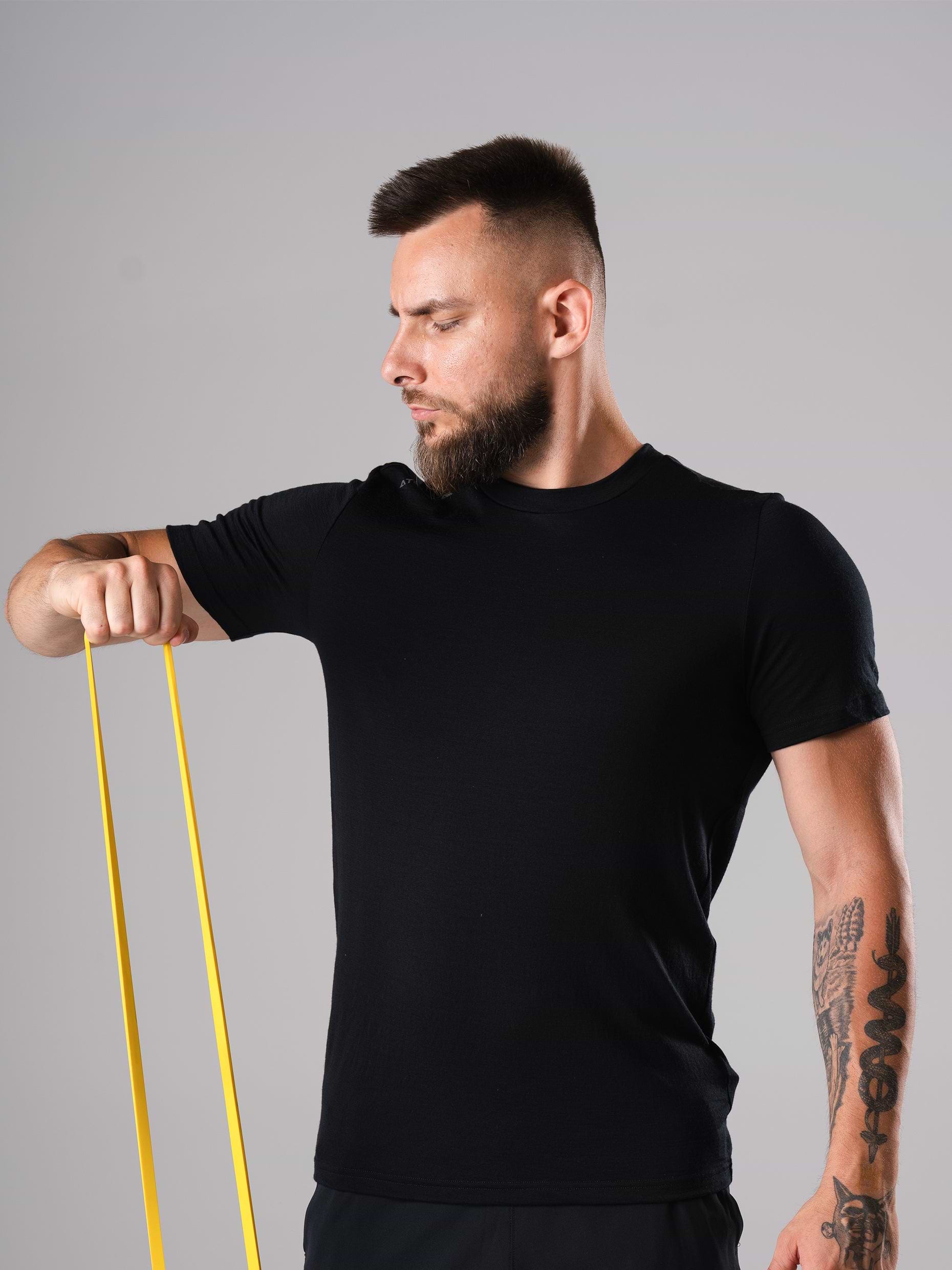 Mann im Ascend Merino Wool T-Shirt in Schwarz von Atletica, beim Training mit gelbem Widerstandsband