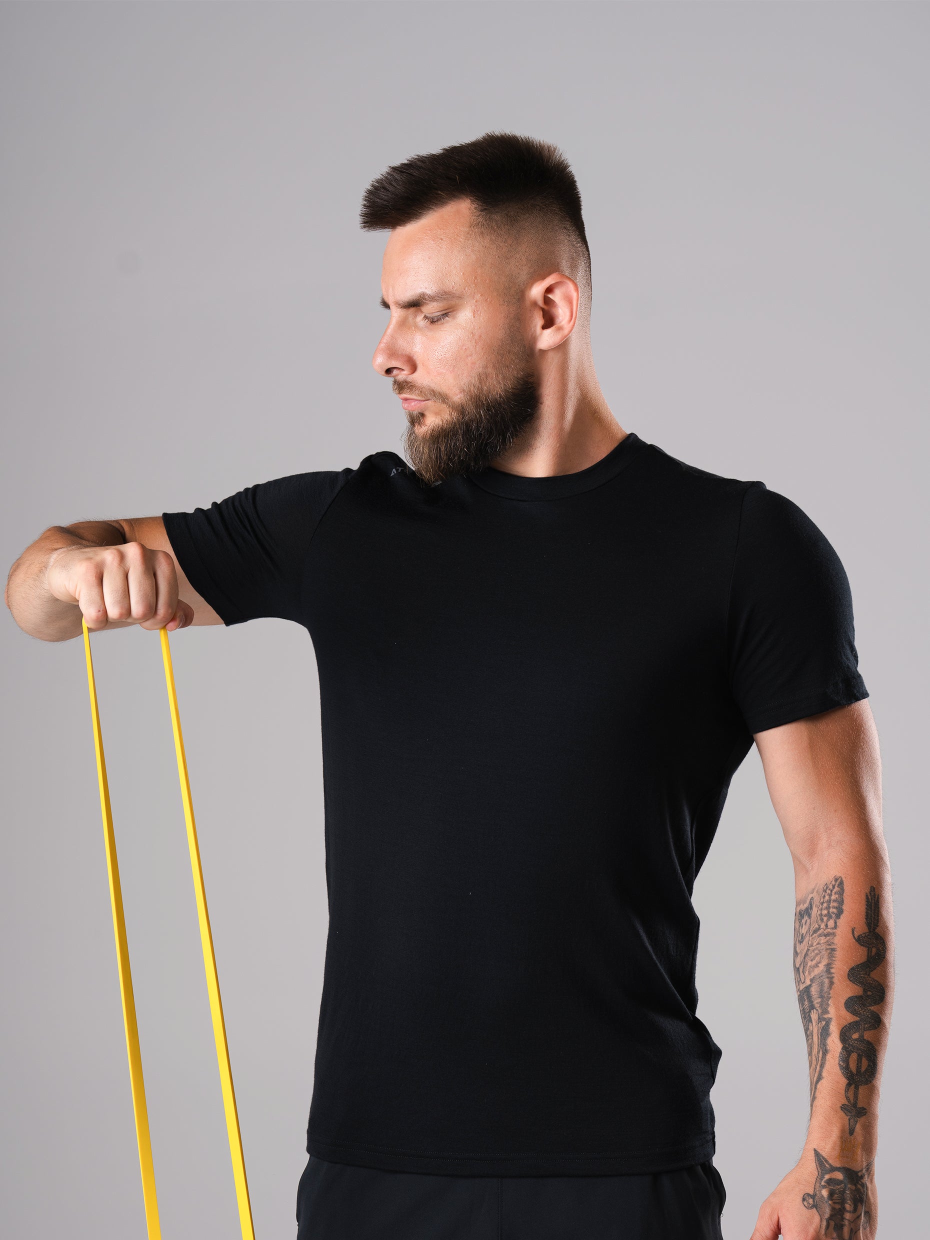 Mann im Ascend Merino Wool T-Shirt in Schwarz von Atletica, beim Training mit gelbem Widerstandsband