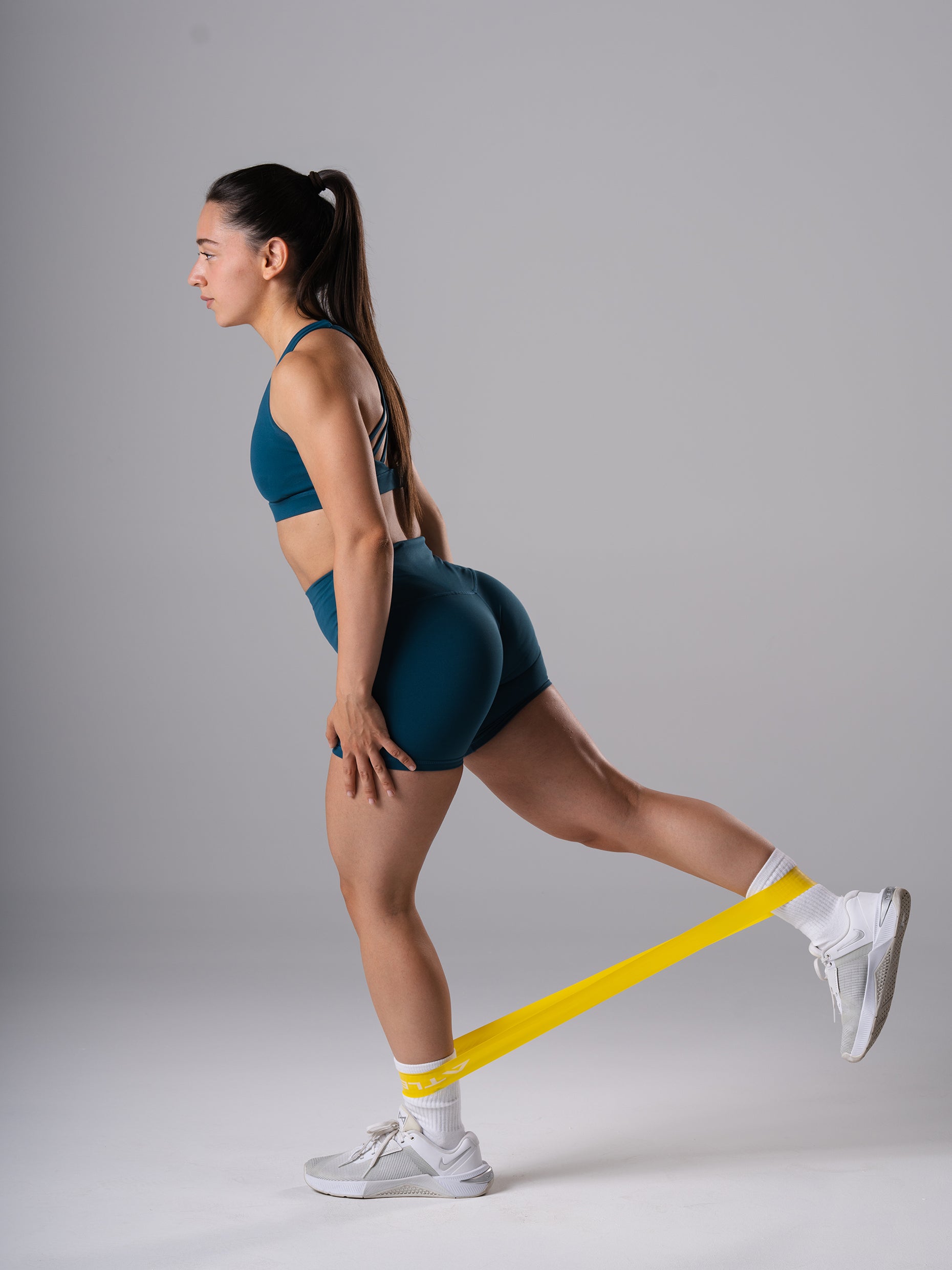 Frau in den Power Form Short Tights in Blue Lagoon von Atletica beim Beintraining mit gelbem Widerstandsband
