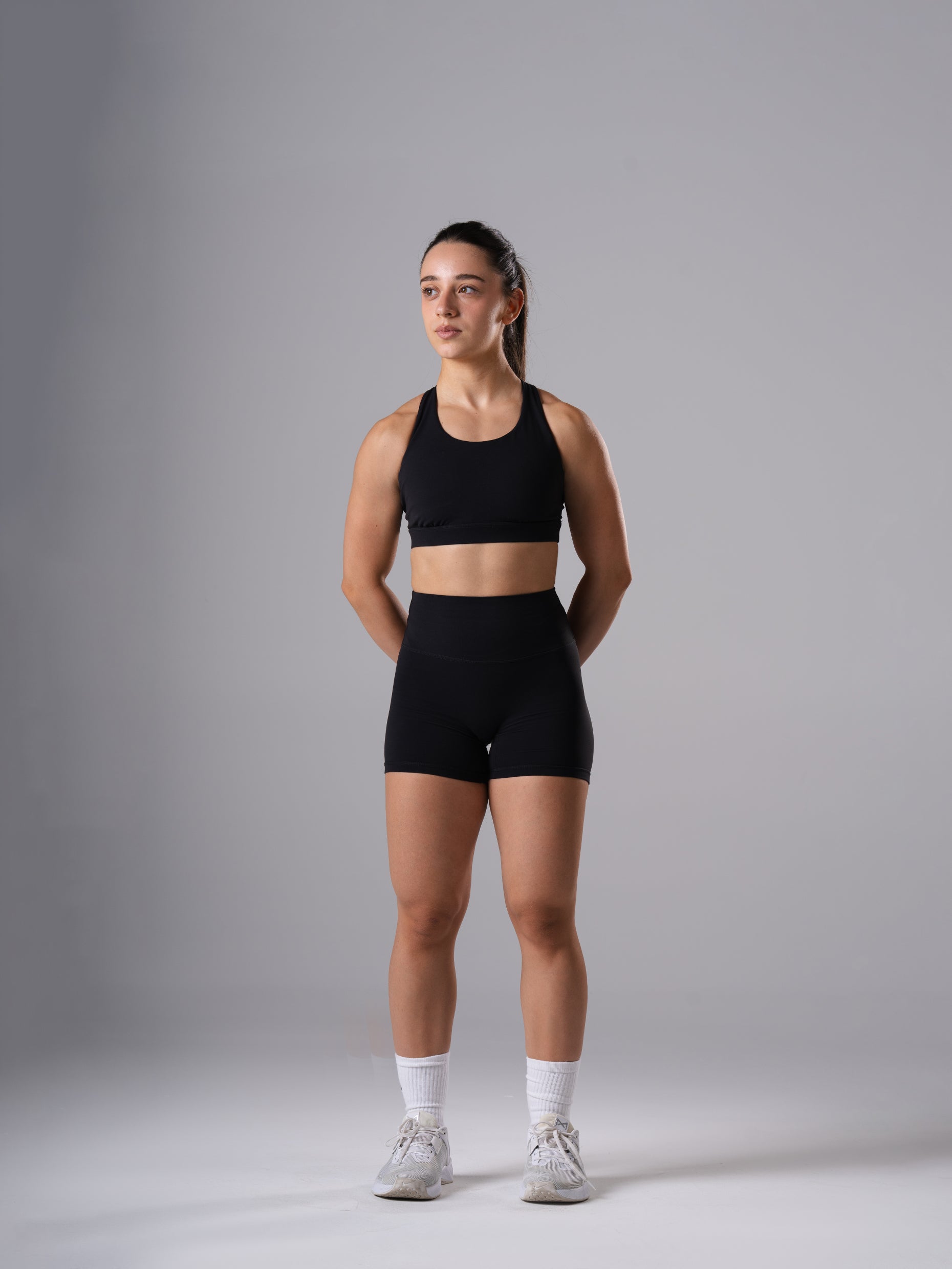 Frau in den Power Form Short Tights in Schwarz von Atletica mit schwarzem Power Form Bra, Ganzkörperansicht