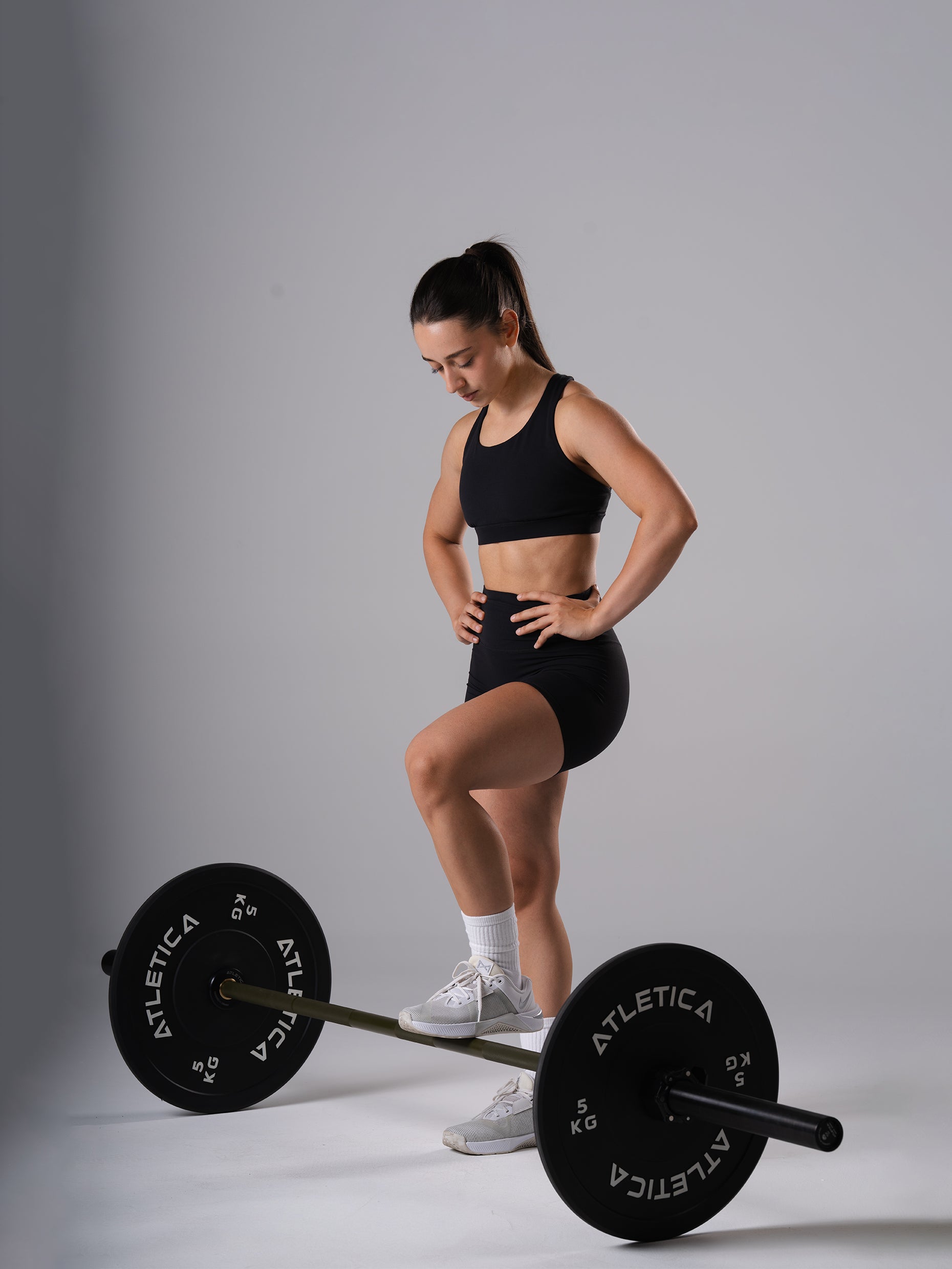 Frau in den schwarzen Power Form Short Tights von Atletica im Halbknien neben einer Langhantel mit Bumper Plates