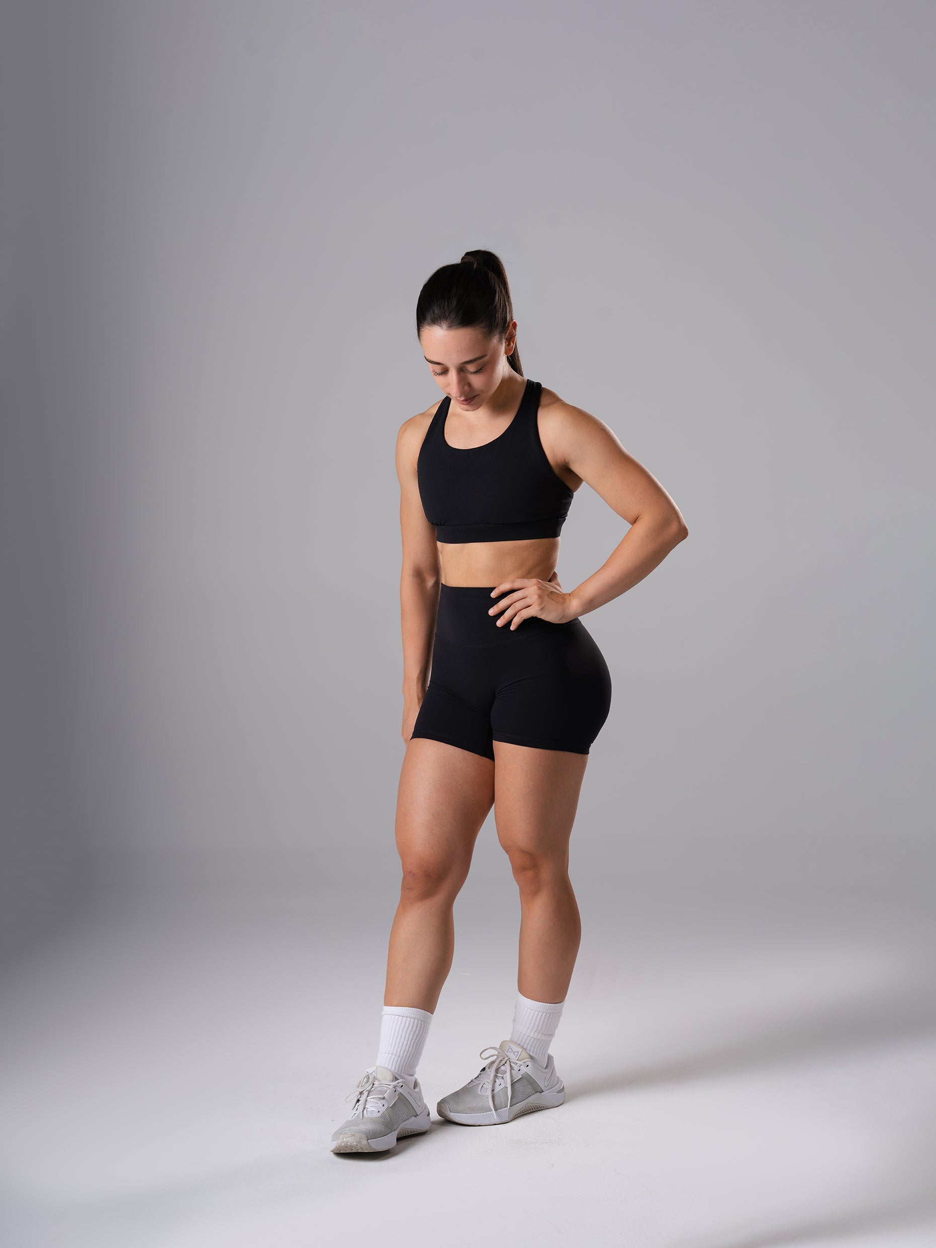 Frau im Power Form Sports Bra in Schwarz von Atletica mit passenden Shorts, schräge Ganzkörperansicht