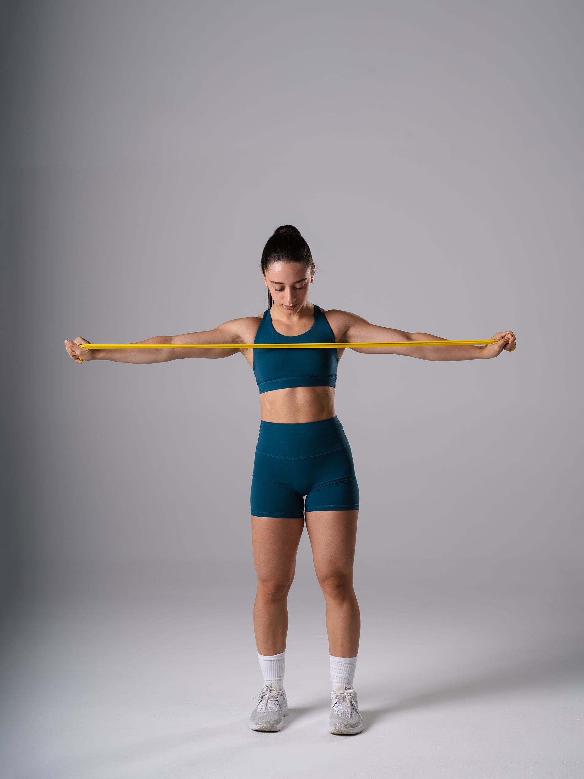 Frau im Power Form Sports Bra in Blue Lagoon von Atletica beim Band Pull-Apart mit Widerstandsband