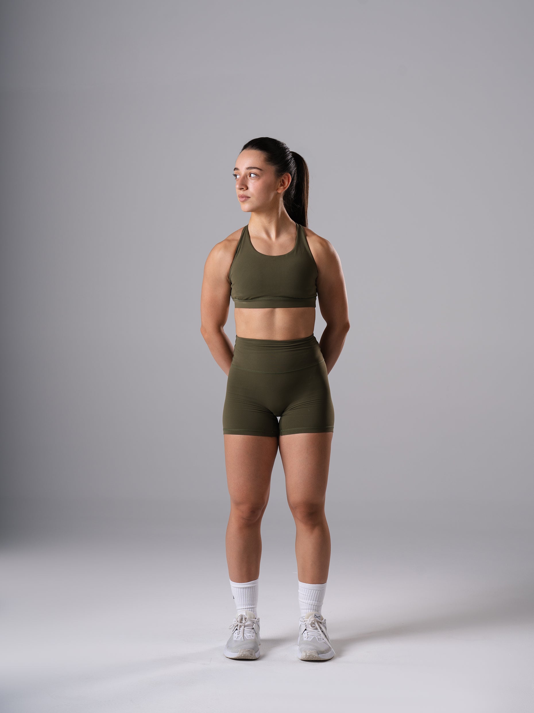 Frau im Power Form Sports Bra in Olive Night von Atletica mit passenden Shorts, Ganzkörperansicht