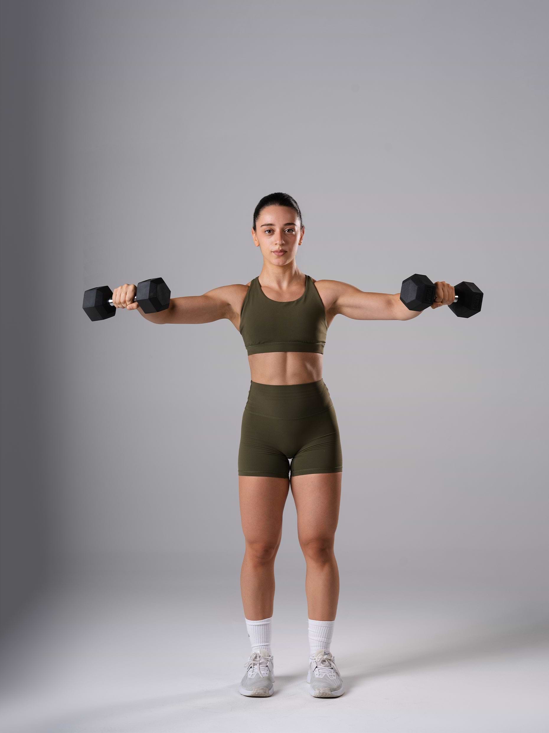 Frau im Power Form Sports Bra in Olive Night von Atletica beim Seitheben mit Atletica Hexagon Kurzhanteln