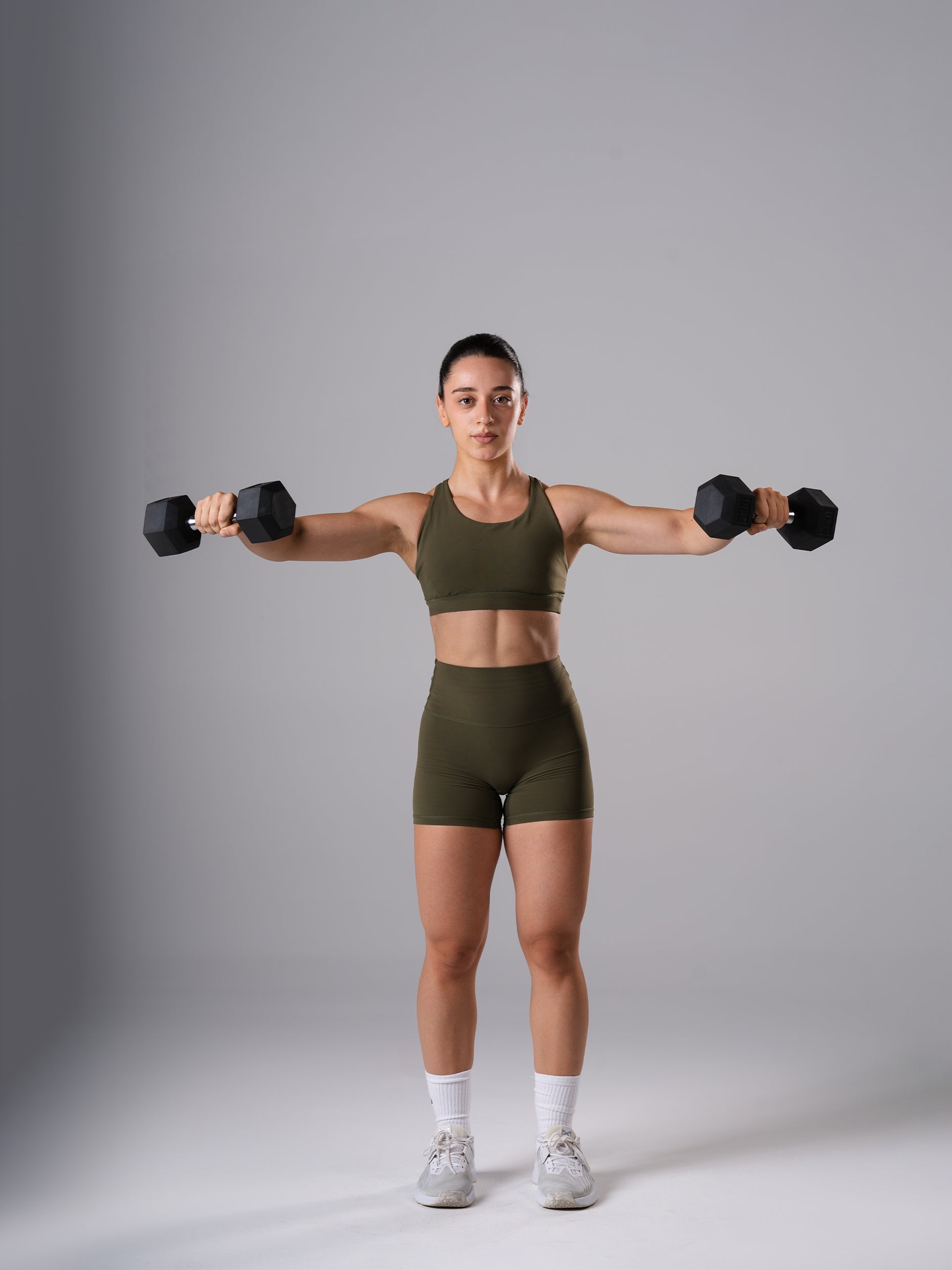 Frau im Power Form Sports Bra in Olive Night von Atletica beim Seitheben mit Atletica Hexagon Kurzhanteln