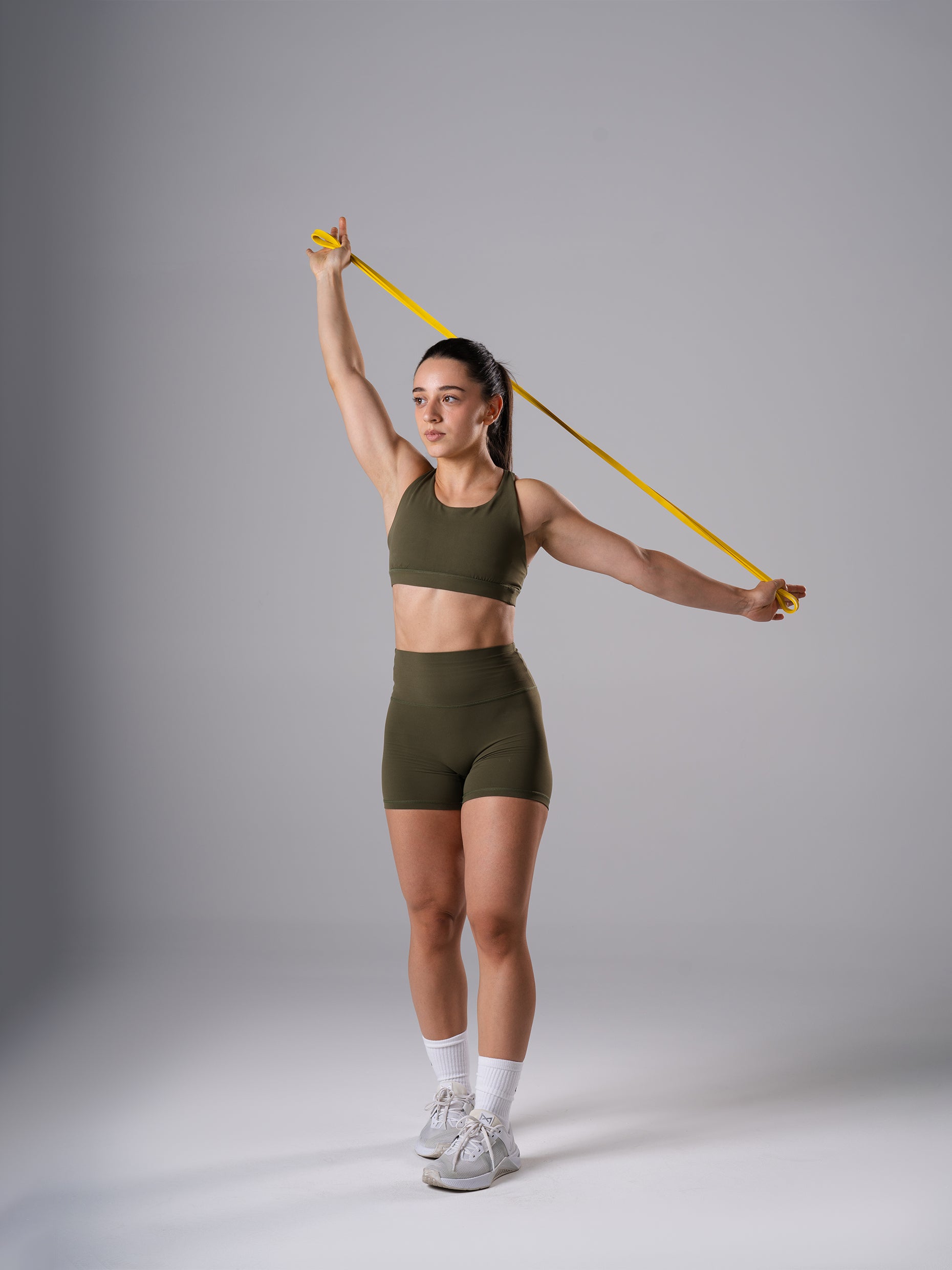 Frau im Power Form Sports Bra in Olive Night von Atletica beim Training mit Widerstandsband über Kopf