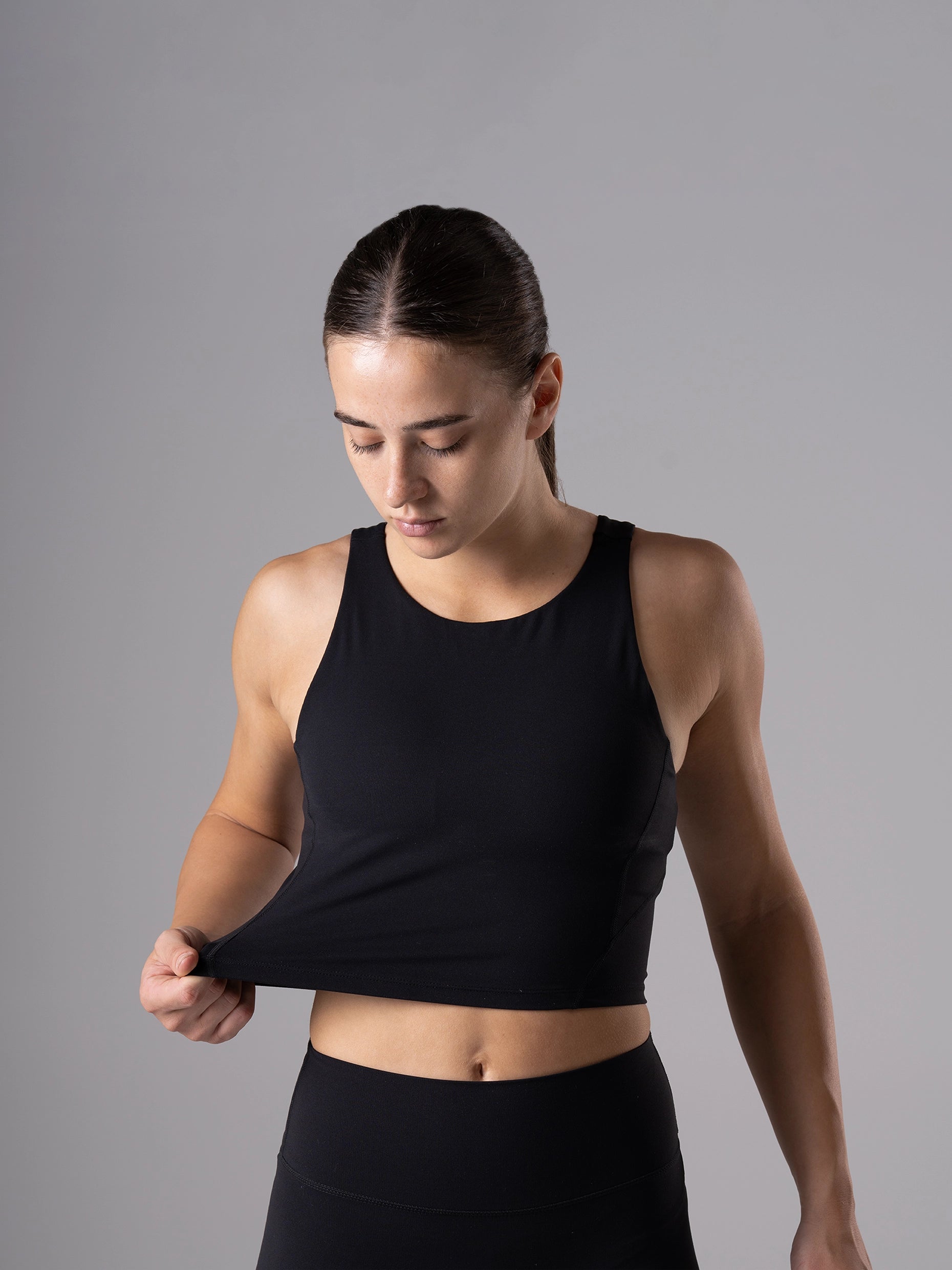 Frau zupft am Saum des schwarzen Power Form Tank Top Bra von Atletica, Detailansicht der Passform