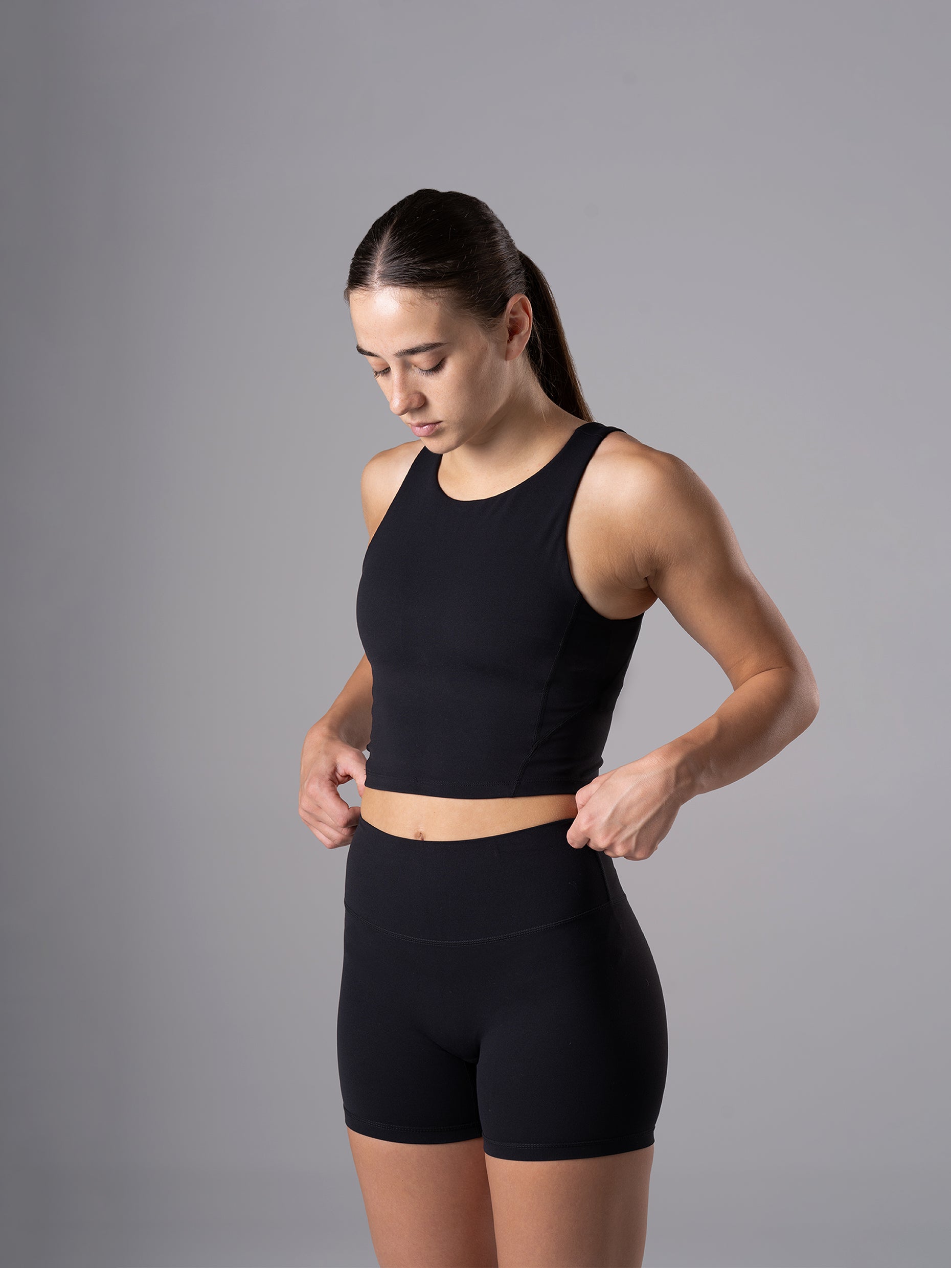 Frau im schwarzen Power Form Tank Top Bra von Atletica rückt den Bund ihrer Shorts zurecht