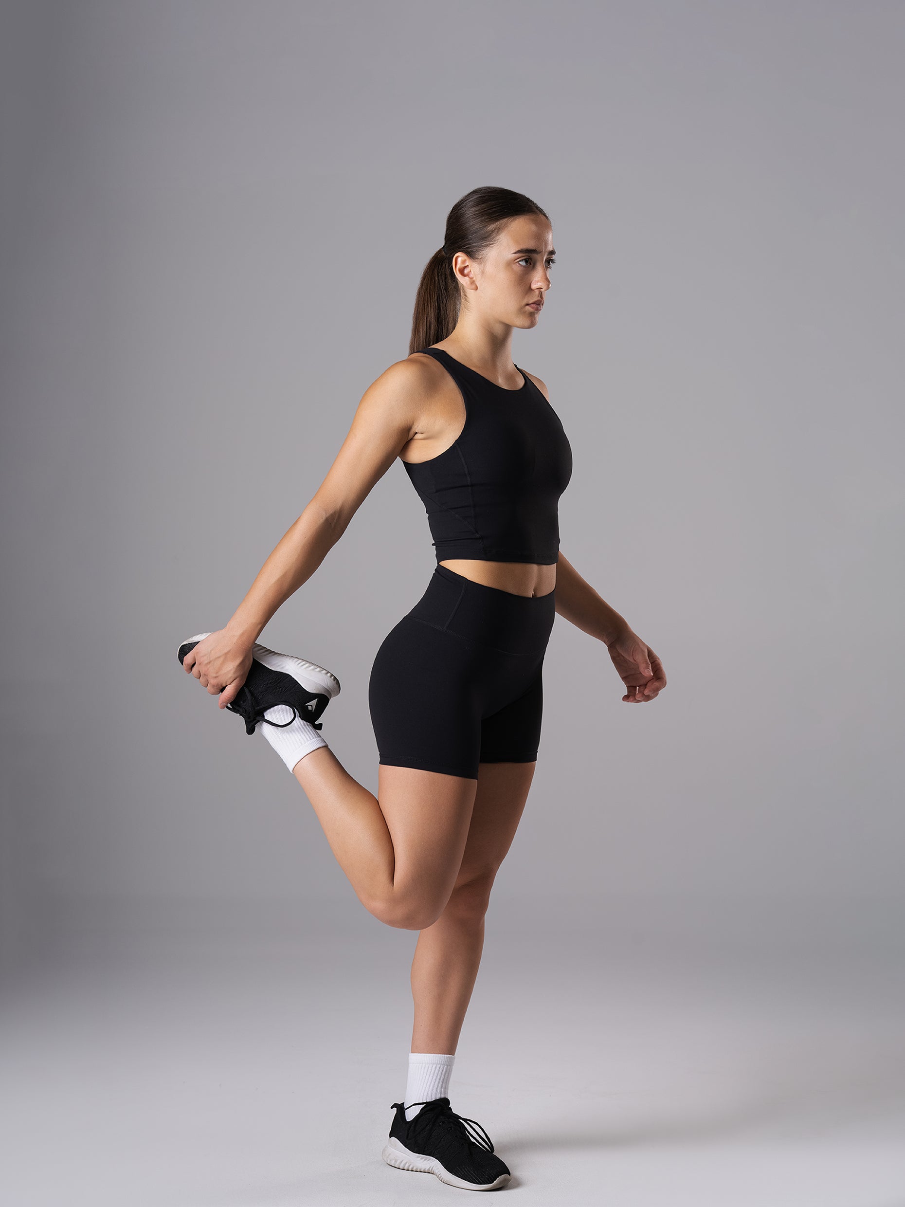 Frau im schwarzen Power Form Tank Top Bra von Atletica beim Dehnen des Oberschenkels im Stand