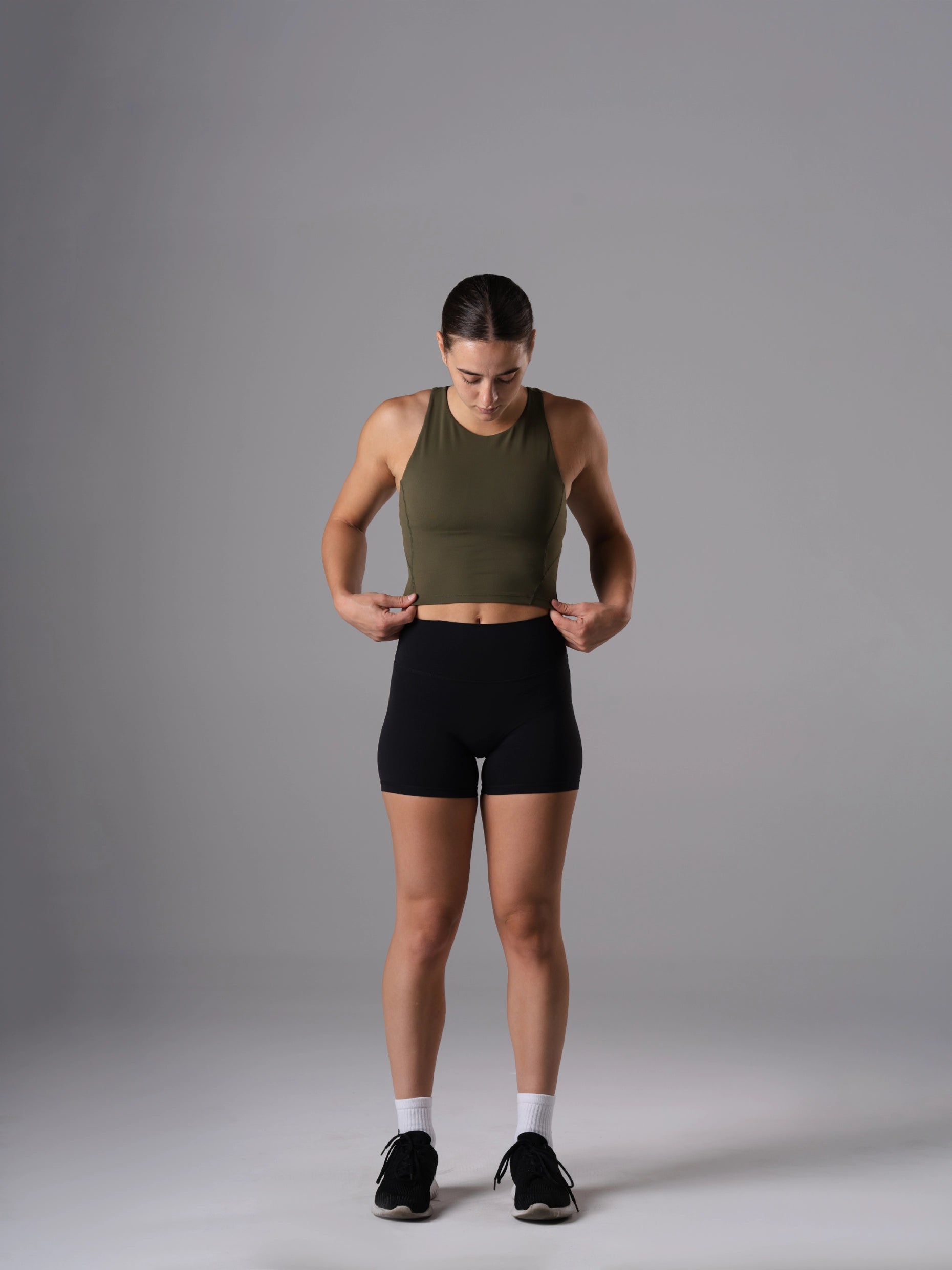 Frau im Power Form Tank Top Bra in Olive Night von Atletica mit schwarzen Shorts, Ganzkörperansicht