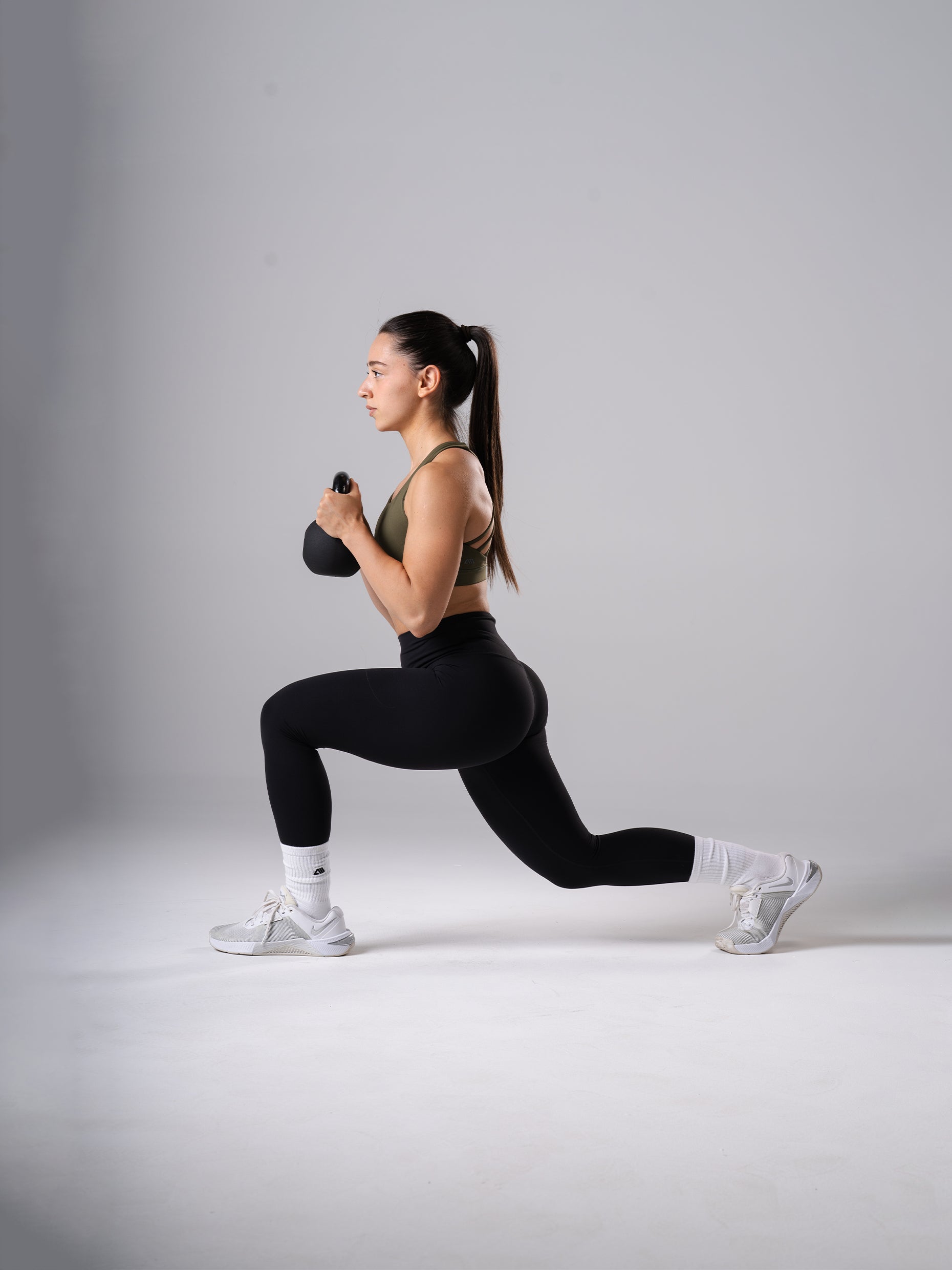 Frau in den schwarzen Power Form Tights von Atletica beim Ausfallschritt mit Kettlebell