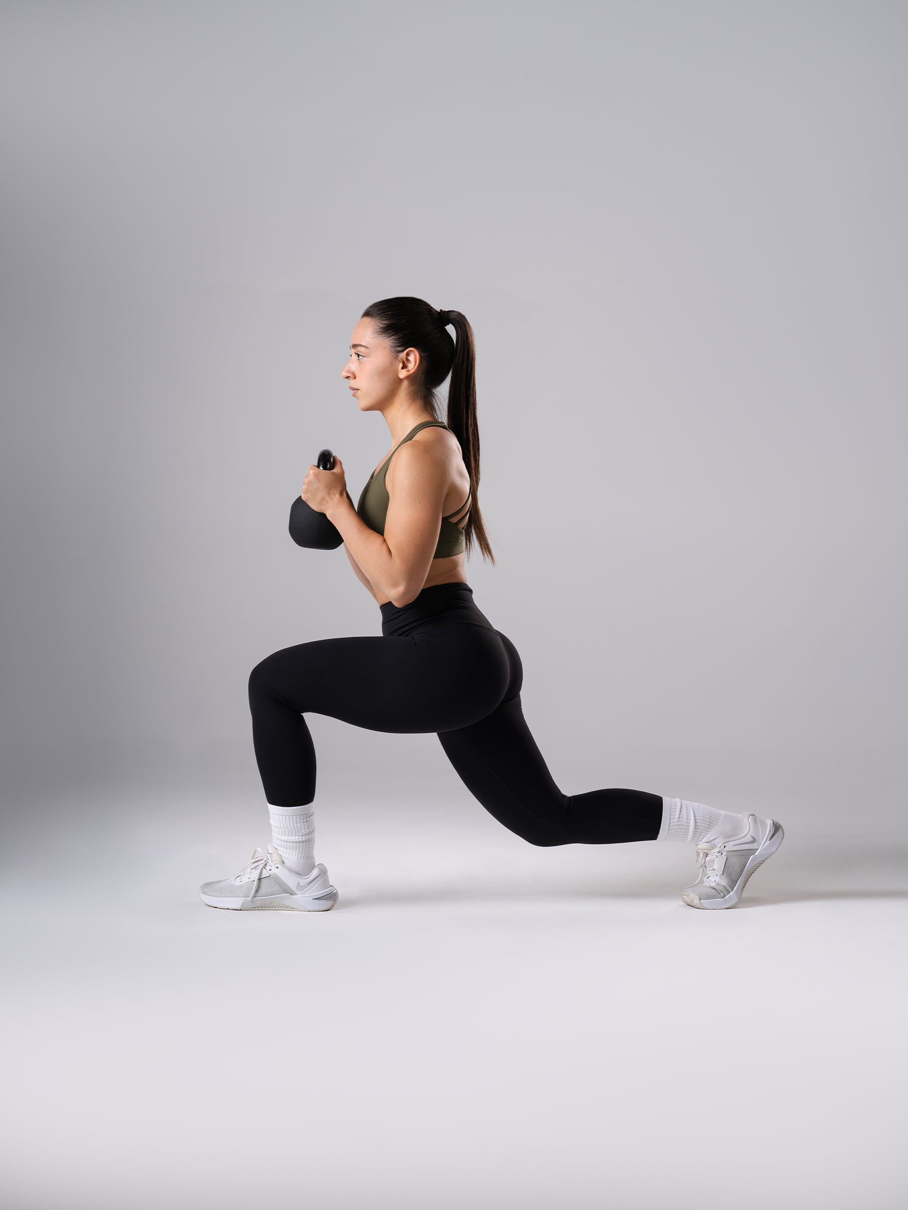 Frau in den schwarzen Power Form Tights von Atletica beim Ausfallschritt mit Kettlebell