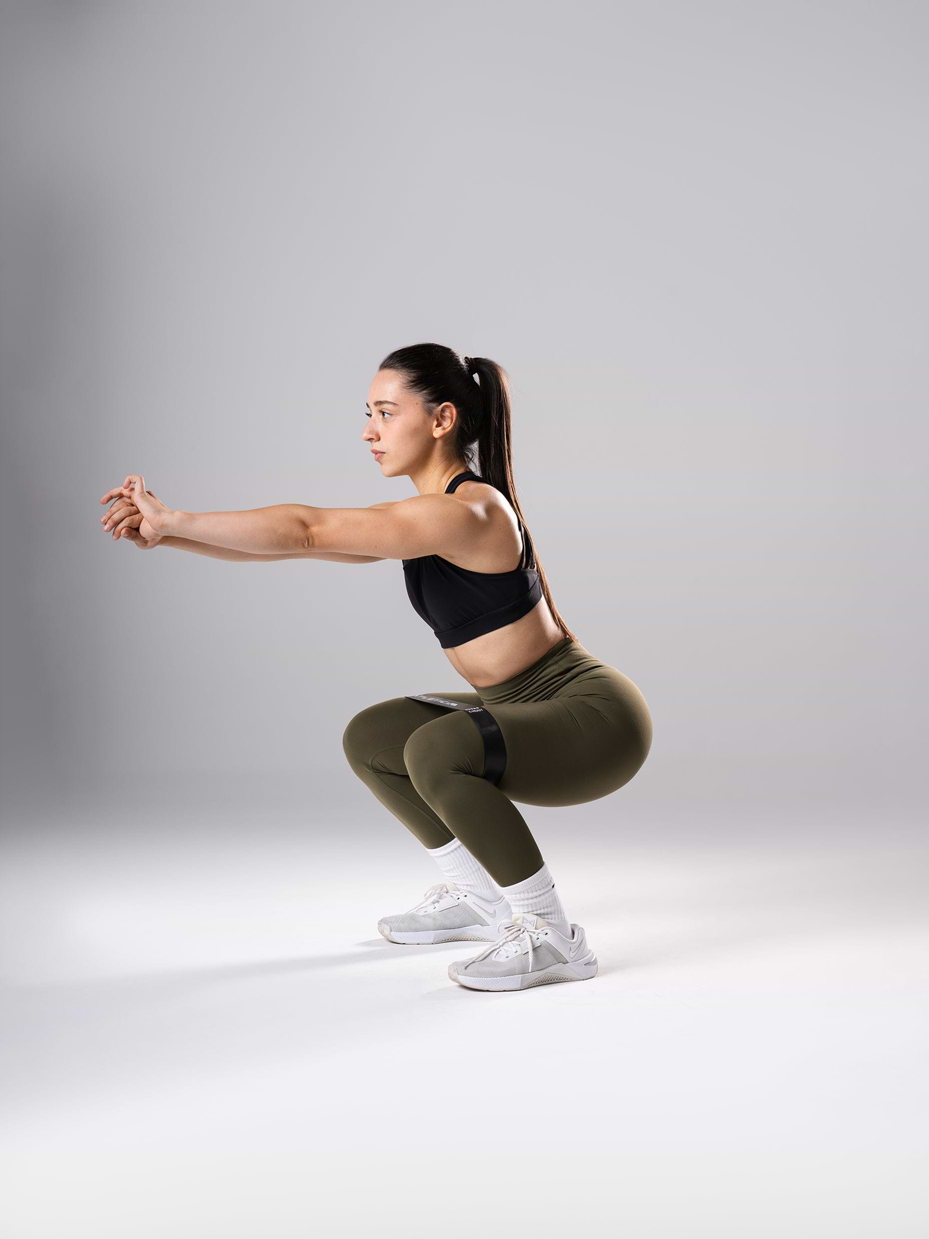 Frau in den Power Form Tights in Olive Night von Atletica bei der Kniebeuge mit Mini Band