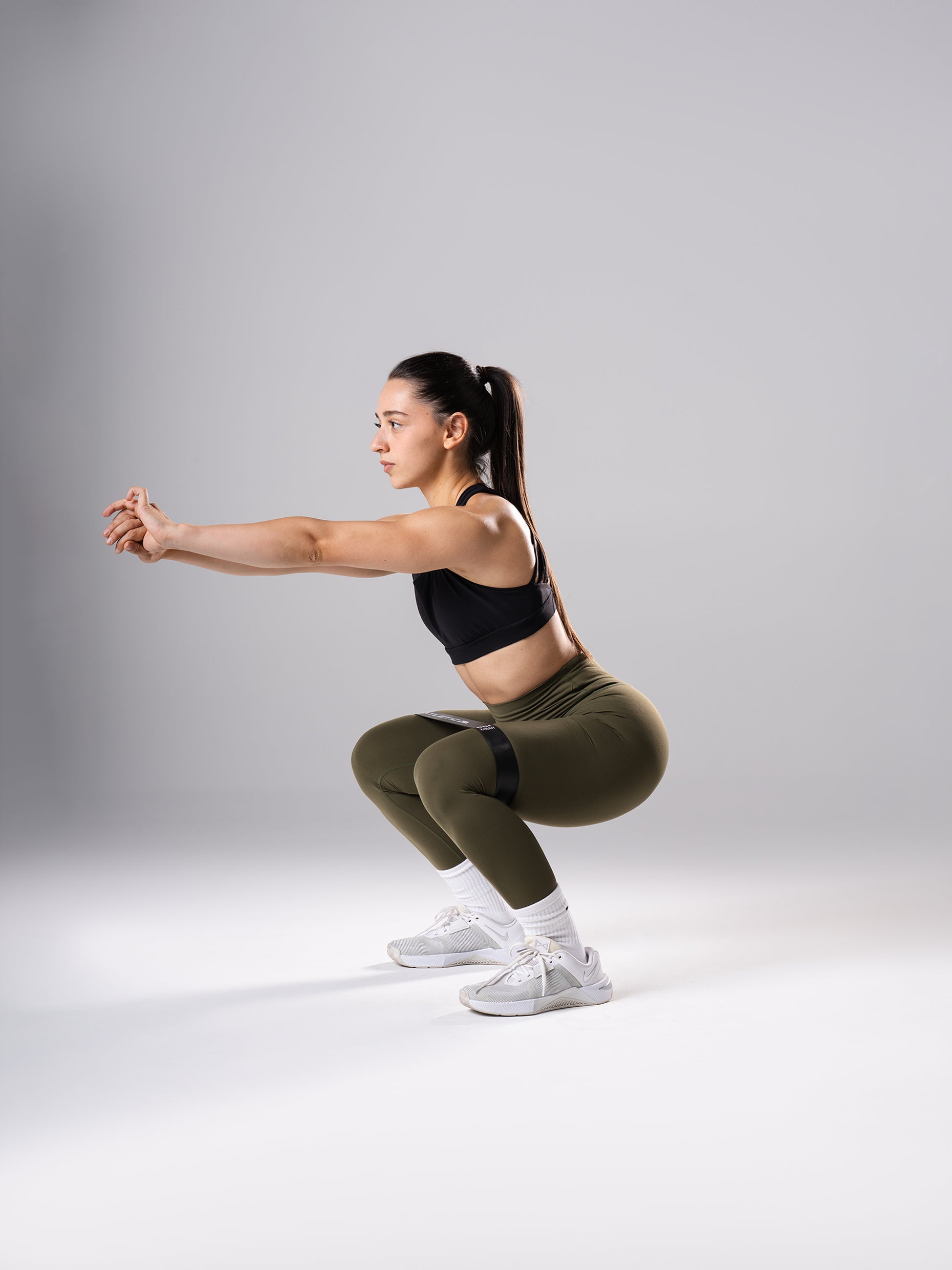 Frau in den Power Form Tights in Olive Night von Atletica bei der Kniebeuge mit Mini Band