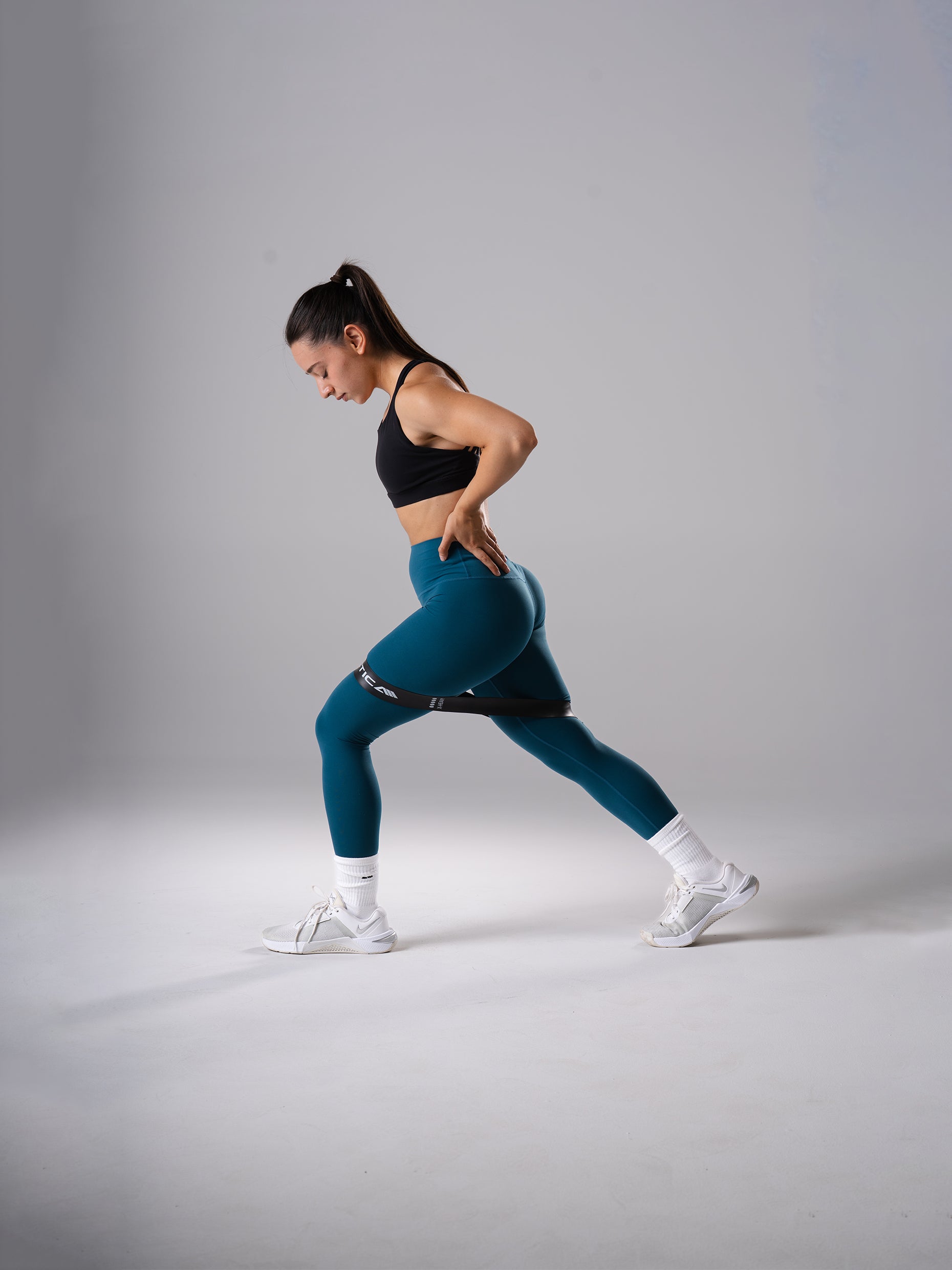 Frau in den Power Form Tights in Blue Lagoon von Atletica beim seitlichen Ausfallschritt mit Widerstandsband