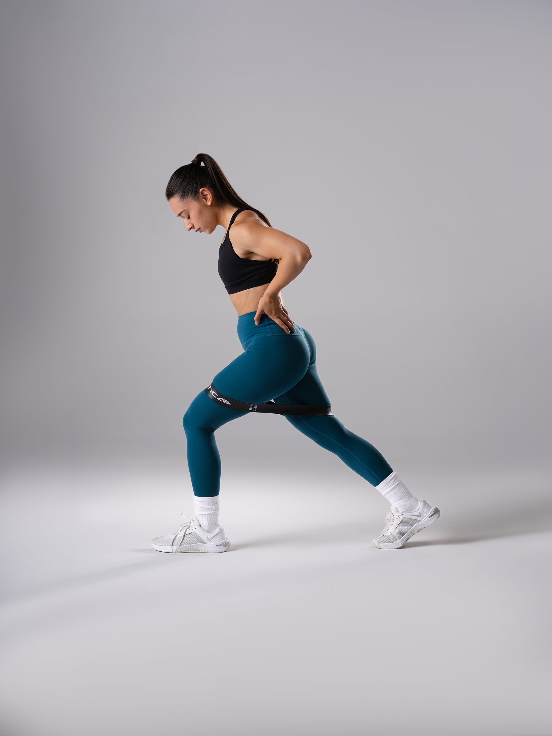 Frau in den Power Form Tights in Blue Lagoon von Atletica beim seitlichen Ausfallschritt mit Widerstandsband