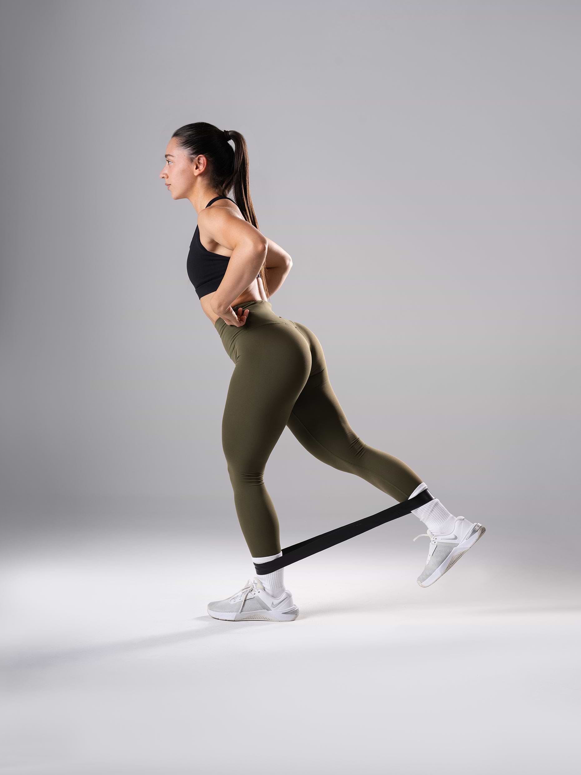 Frau in den Power Form Tights in Olive Night von Atletica beim Beintraining mit Mini Band