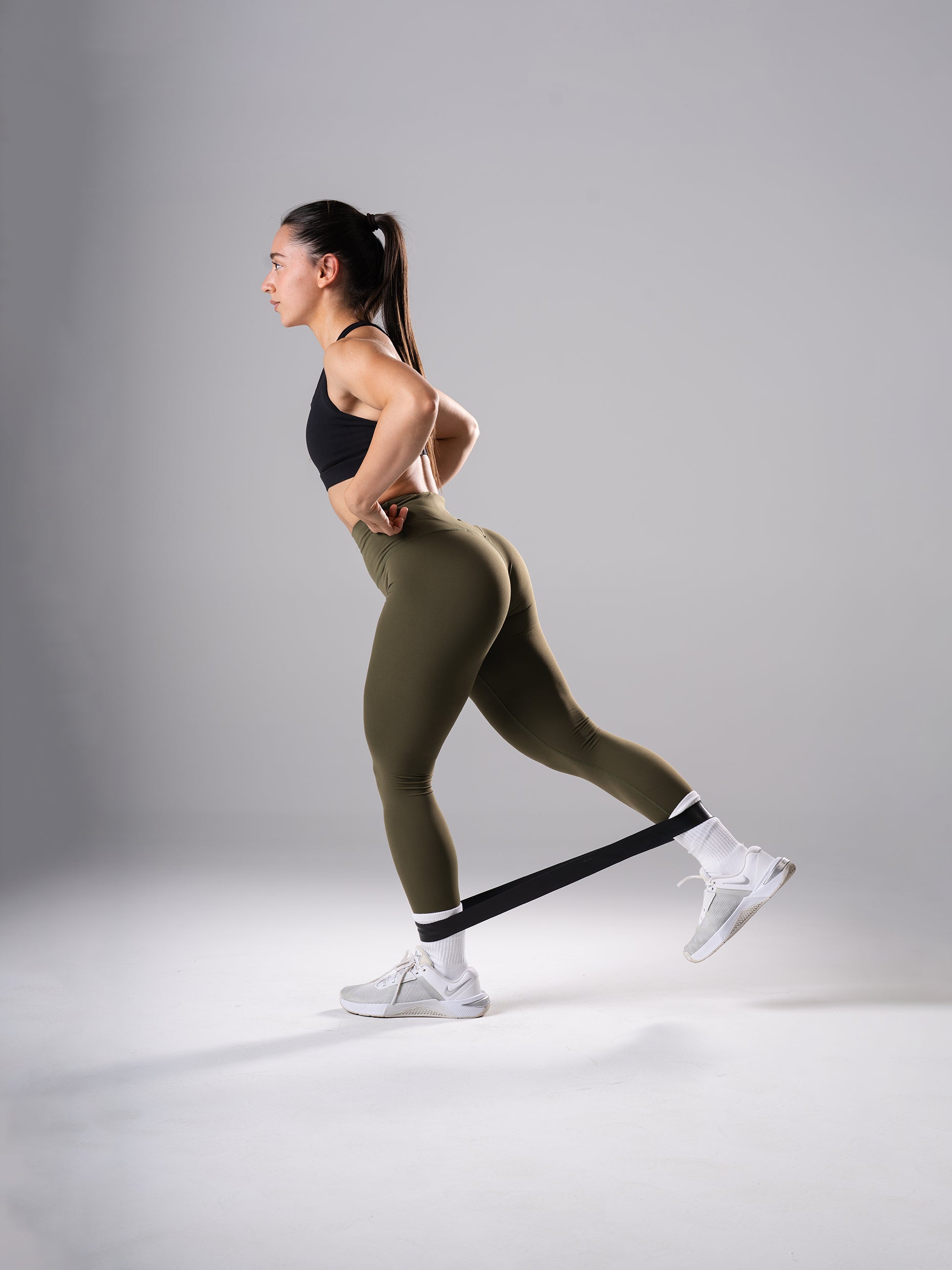 Frau in den Power Form Tights in Olive Night von Atletica beim Beintraining mit Mini Band