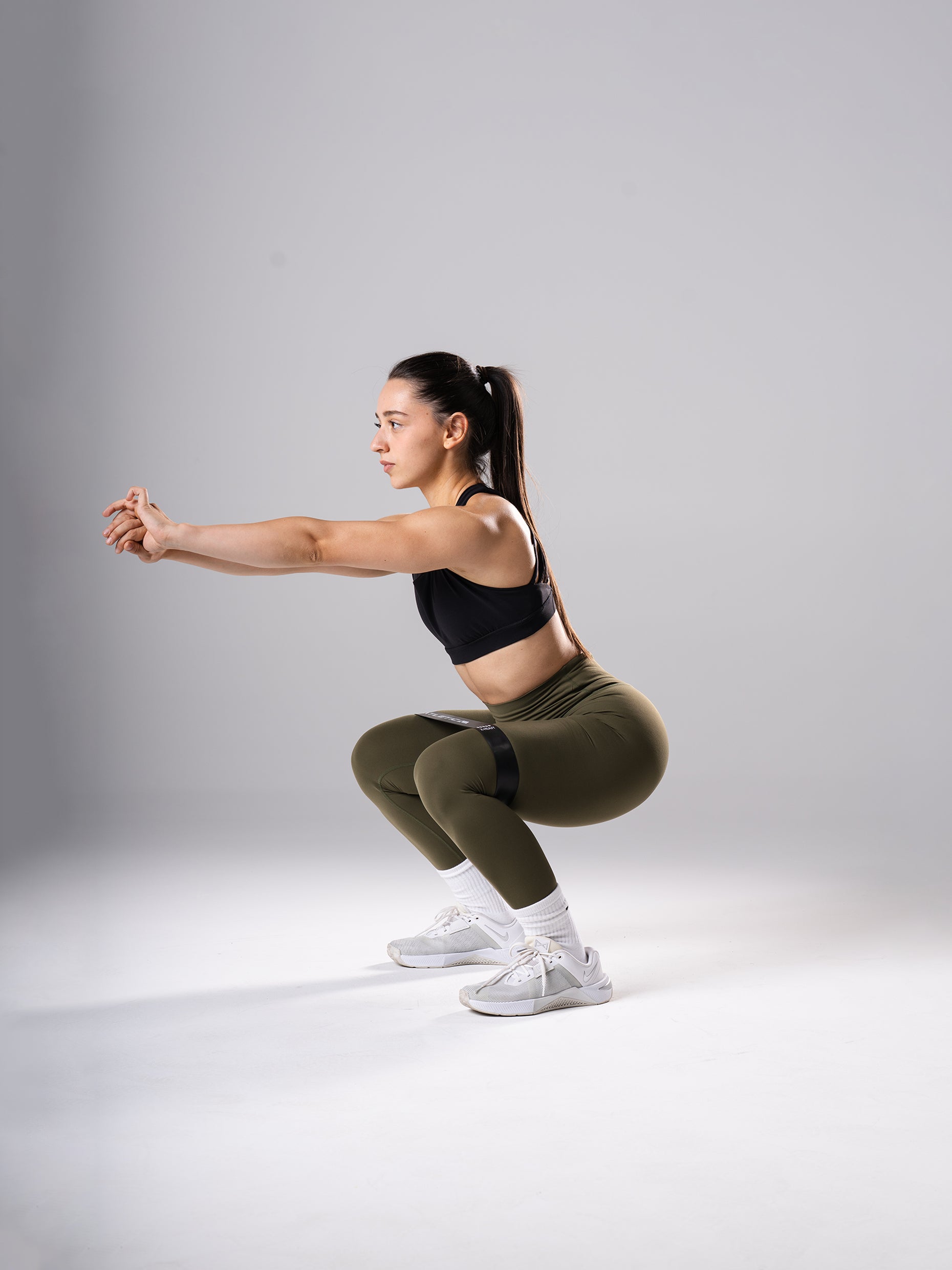 Frau in den Power Form Tights in Olive Night von Atletica bei der Kniebeuge mit Mini Band