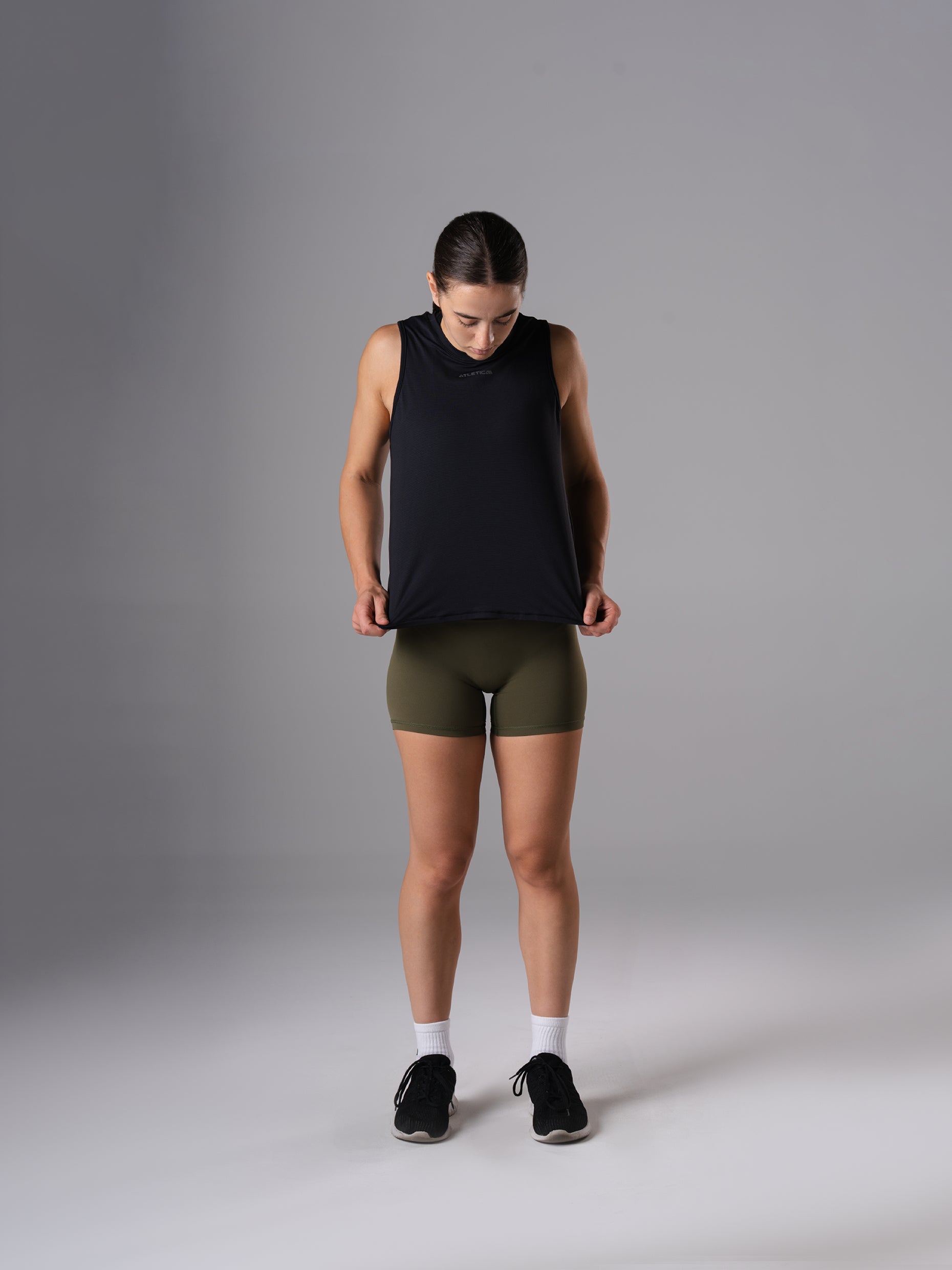 Ganzkörperansicht: Frau im Power Lift Tank Top in Schwarz von Atletica mit olivgrünen Shorts