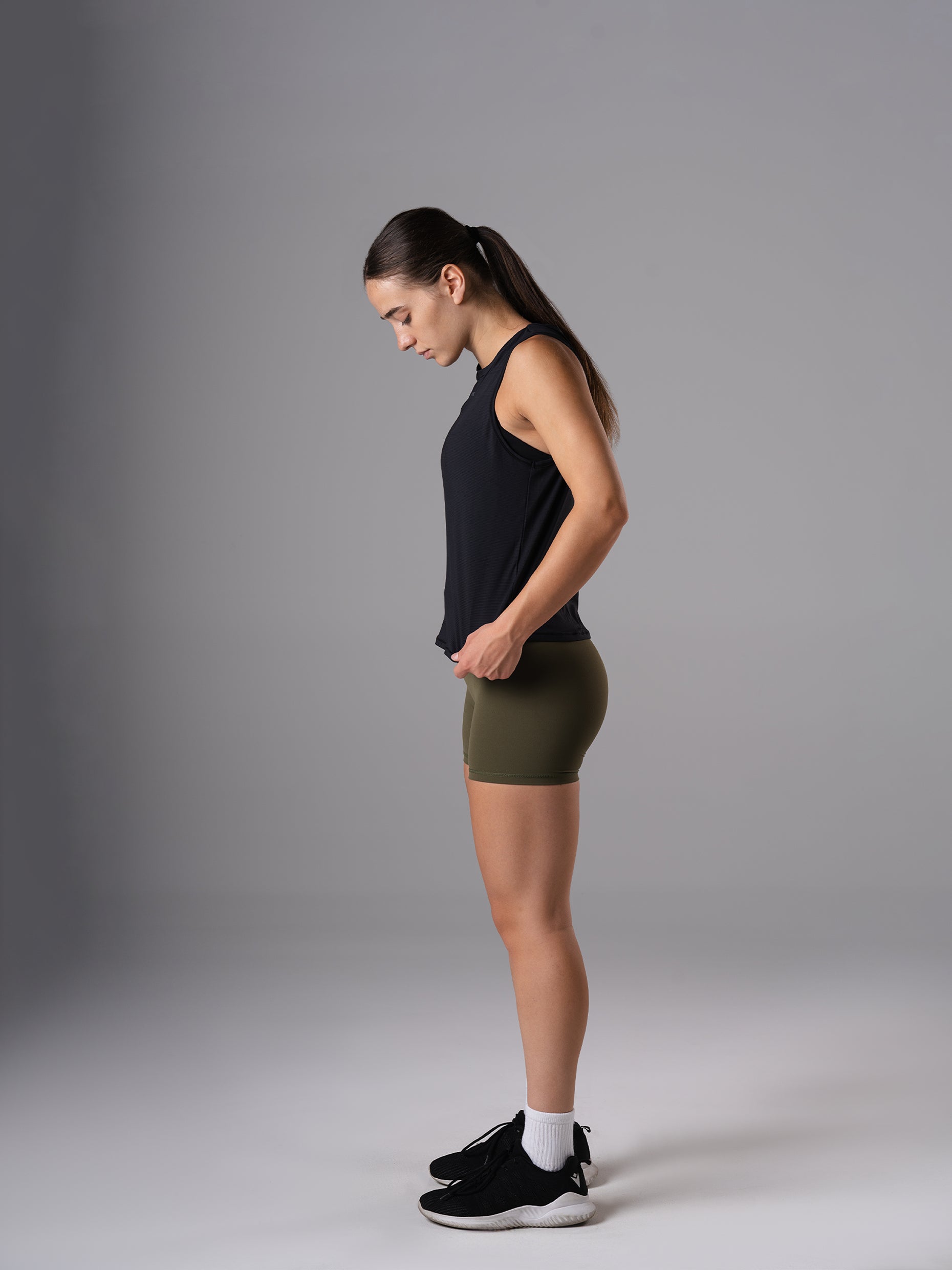 Seitenansicht: Frau im Power Lift Tank Top in Schwarz von Atletica mit olivgrünen Shorts