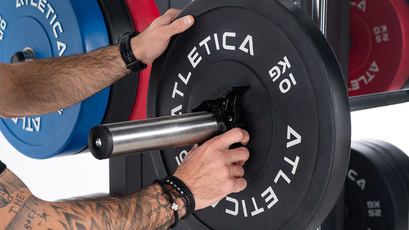 Athlet belädt die Multipresse-Stange mit schwarzen Atletica Bumper Plates und Hantelverschlüssen
