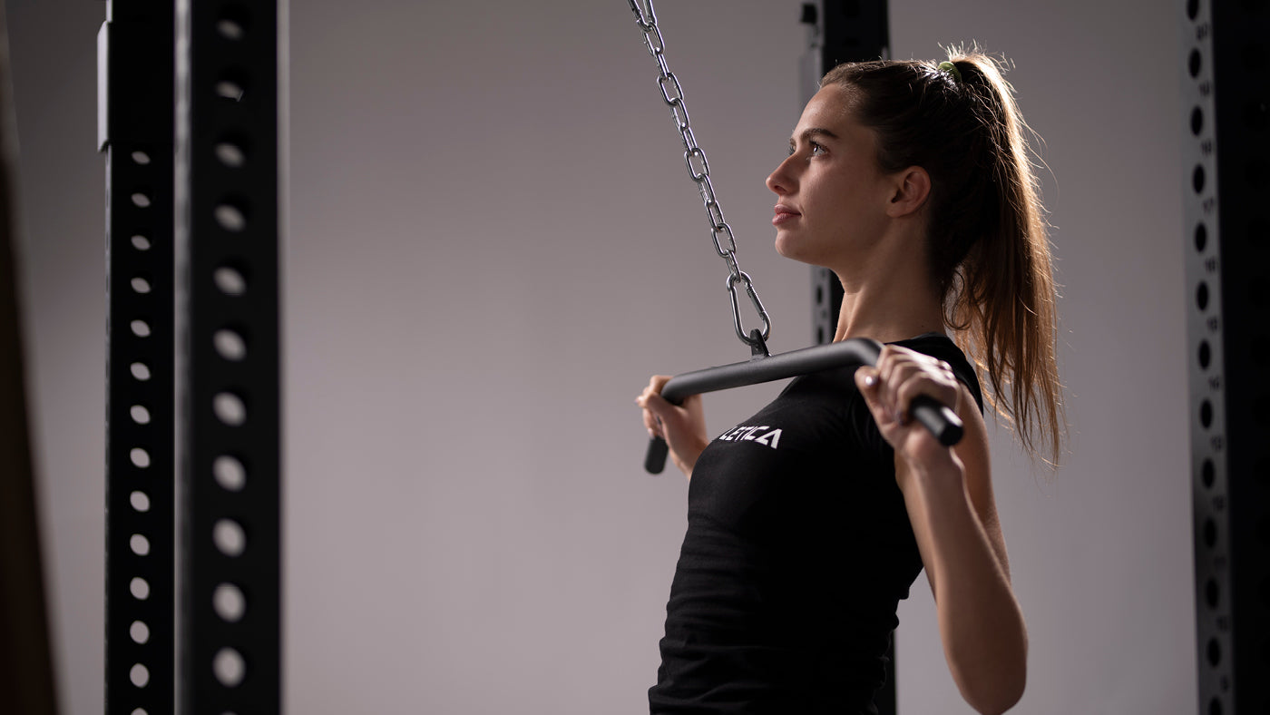 Une femme au tirage vertical devant avec une barre de tirage à la poulie du Power Rack R8