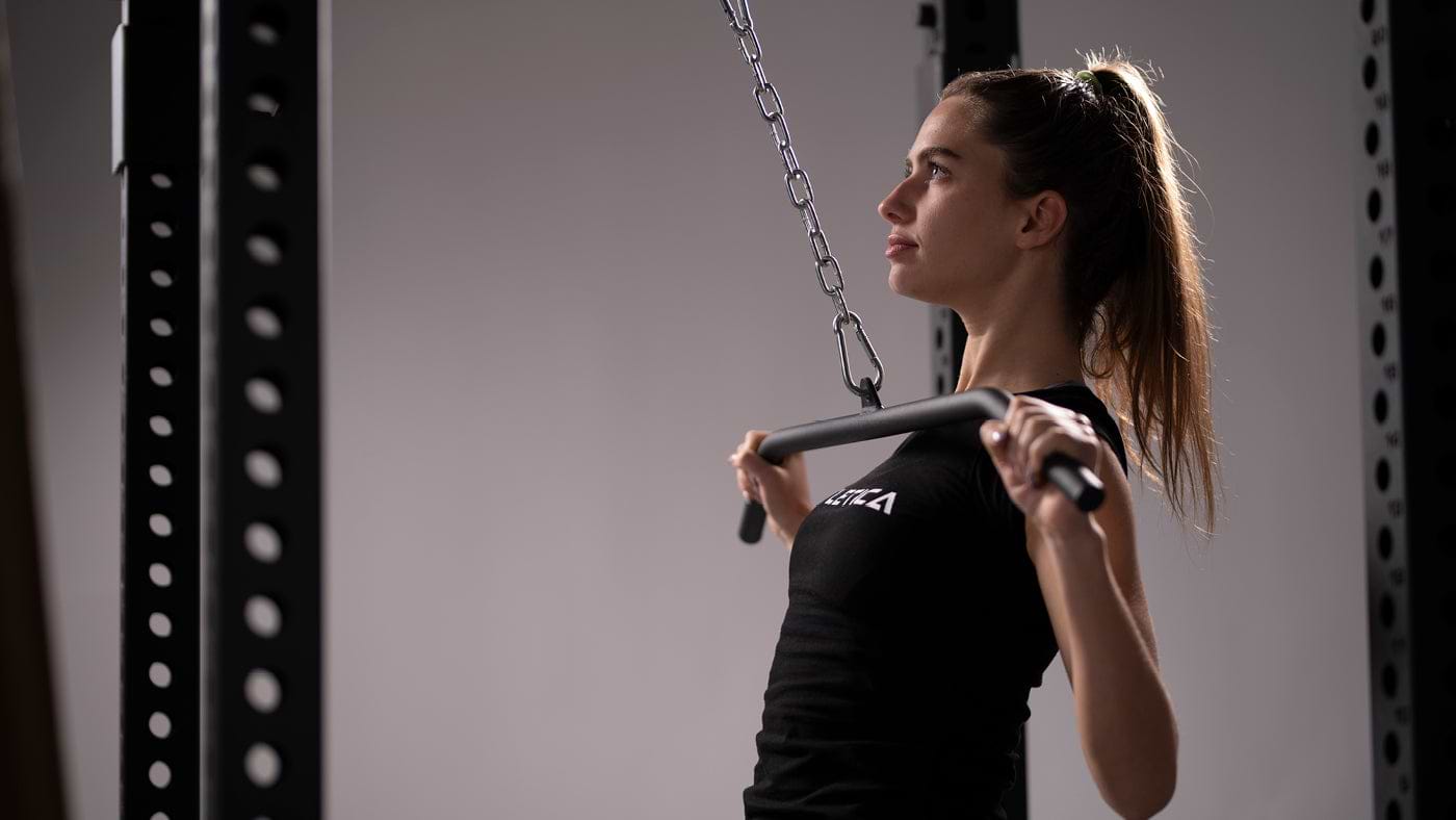 Une femme au tirage vertical devant avec une barre de tirage à la poulie du Power Rack R8