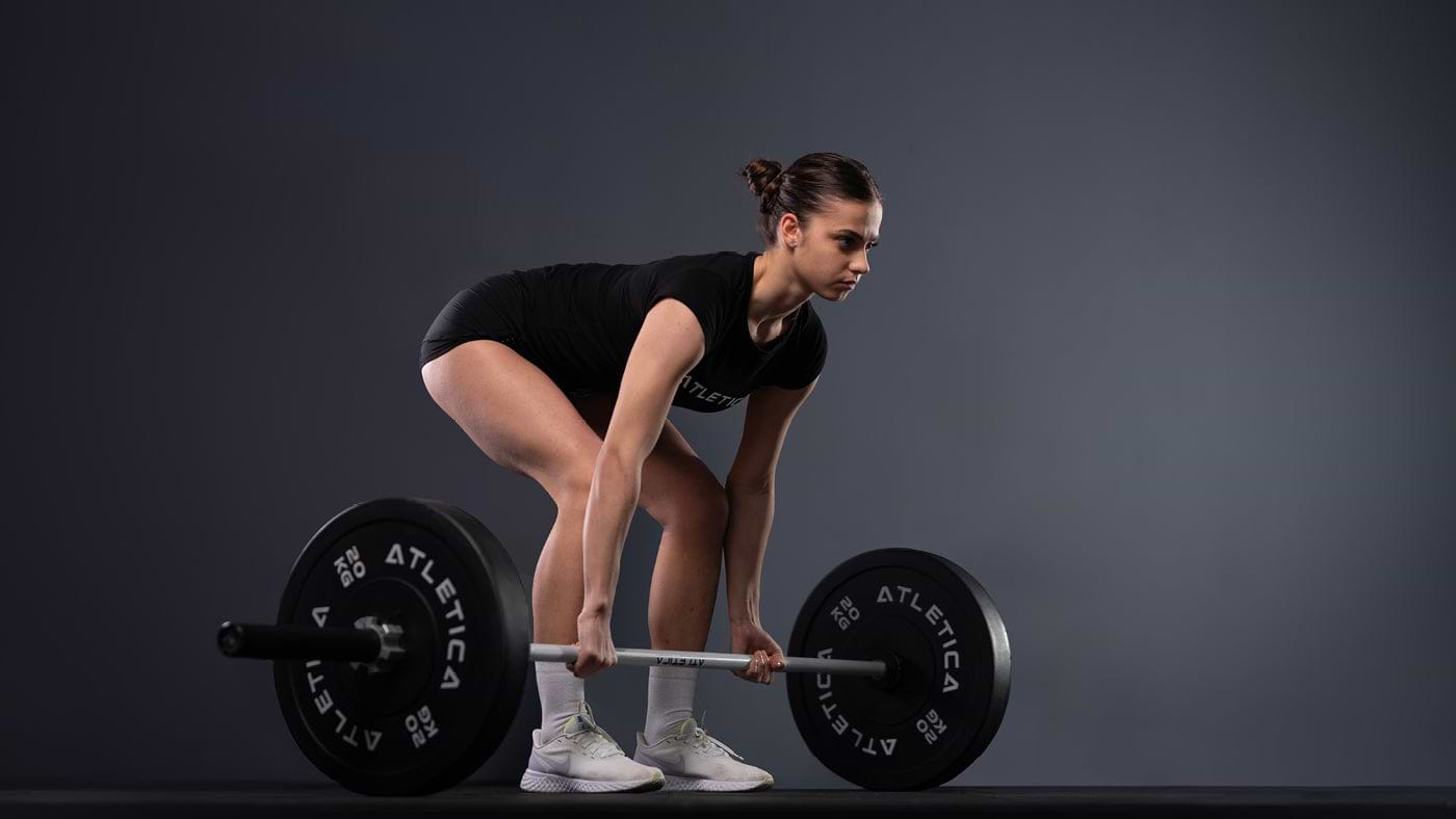Une athlète au soulevé de terre avec une barre Atletica et des disques bumper noirs